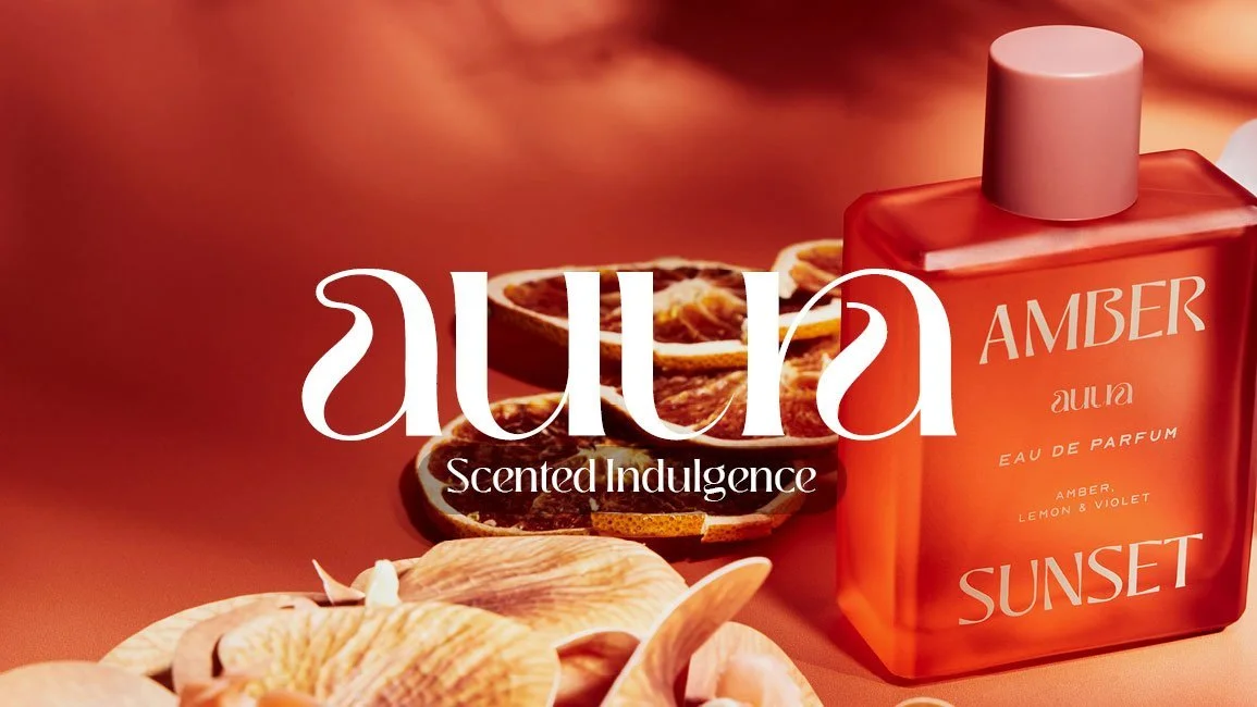 A bottle of Aura Amber Sunset perfume with dried orange slices and seashells in the background.