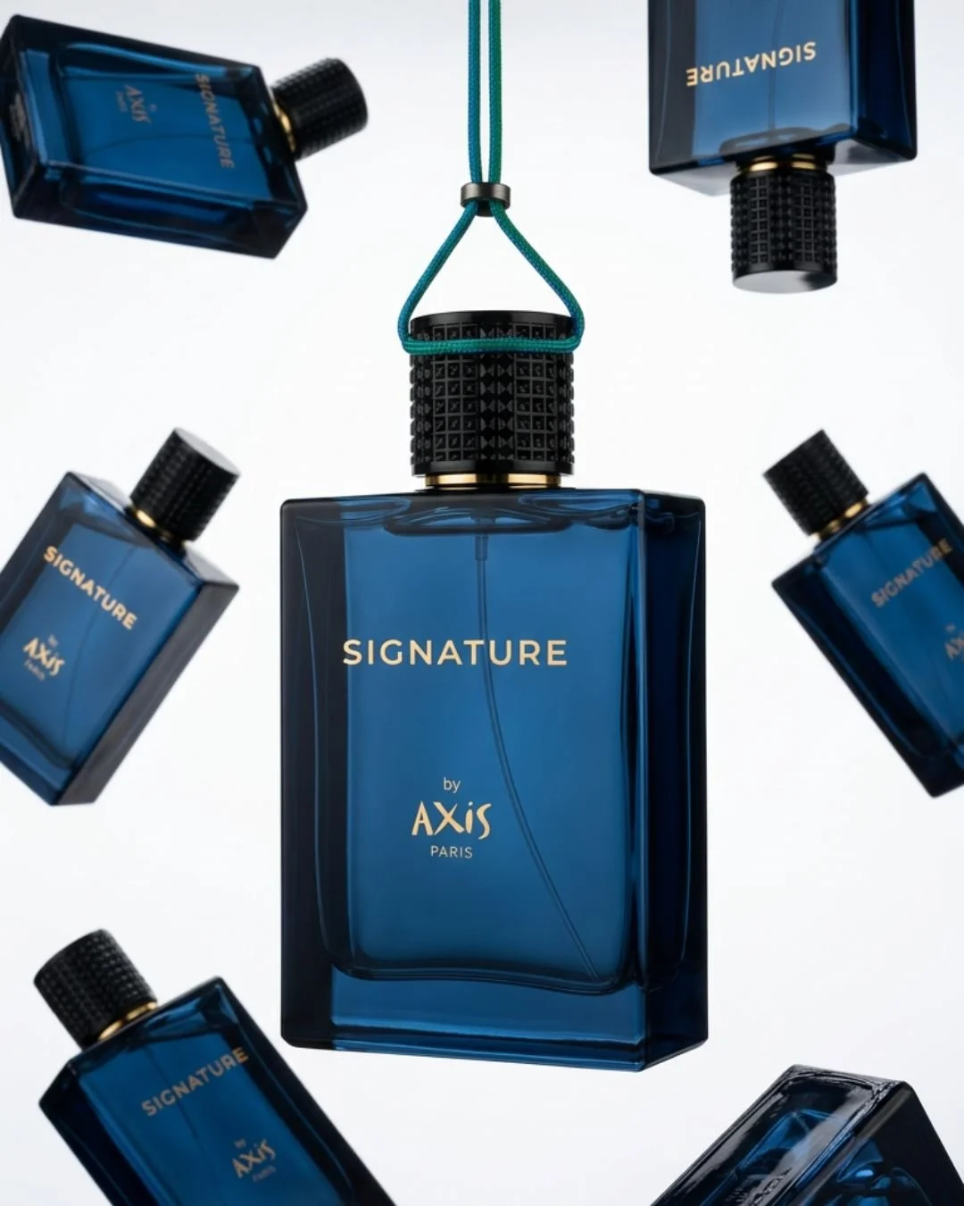 A collection of blue rectangular perfume bottles labeled 'Signature by Axis Paris,' with one bottle hanging by a teal strap and the others floating around on a white background.
