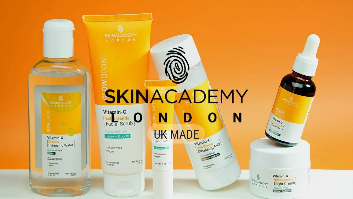 Collection of skincare products from Skin Academy London, including Vitamin C cleansing water, a glow boost facial scrub, eye cream, cleansing milk, and night cream, arranged on a white surface against an orange background.