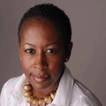 A portrait of Julia Coney smiling at the camera with a gold necklace and white blouse