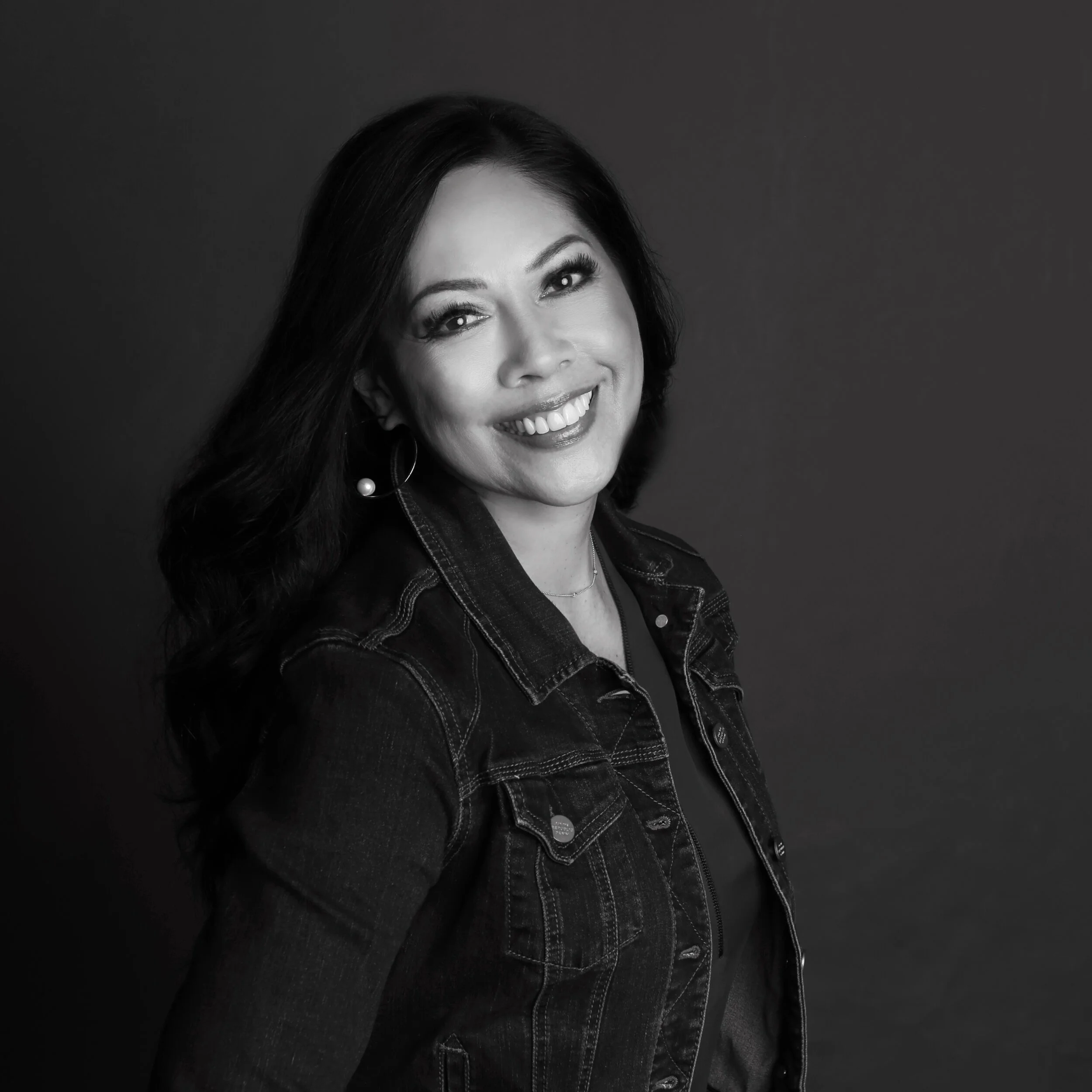 A black and white portrait of Annette Alvarez-Peters smiling in a denim jacket