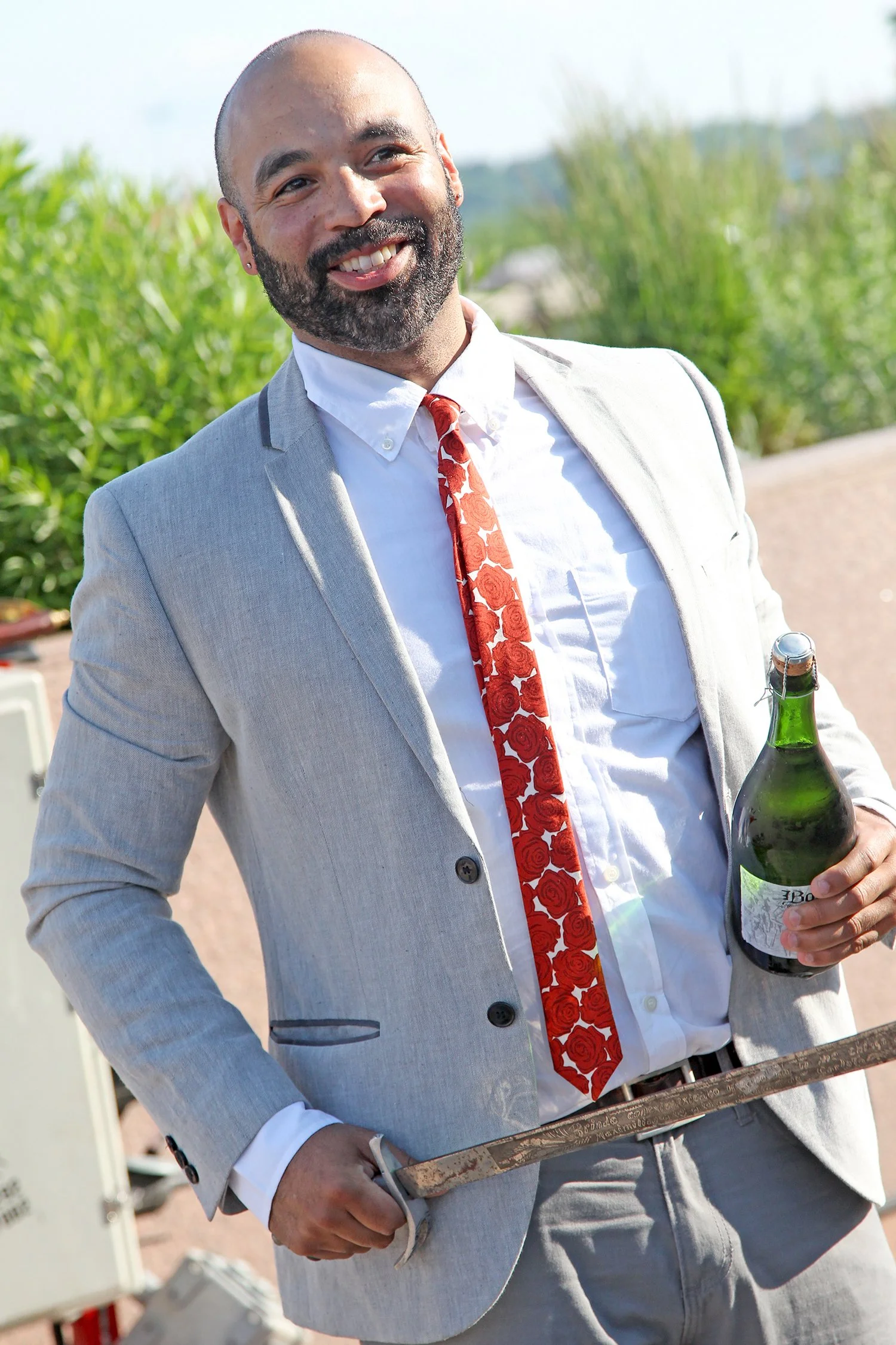 Chris Christensen smiling outdoors, holding a bottle of wine