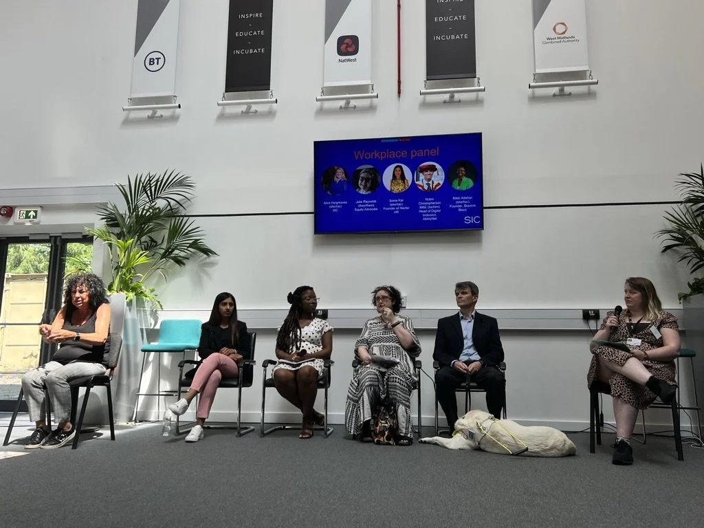 A photo of the SIC conference. It shows a panel of disabled people speaking, hosted by Alice, SIC's CEO,  with a screen showing their headshots behind them. A BSL interpreter is to the left of them.