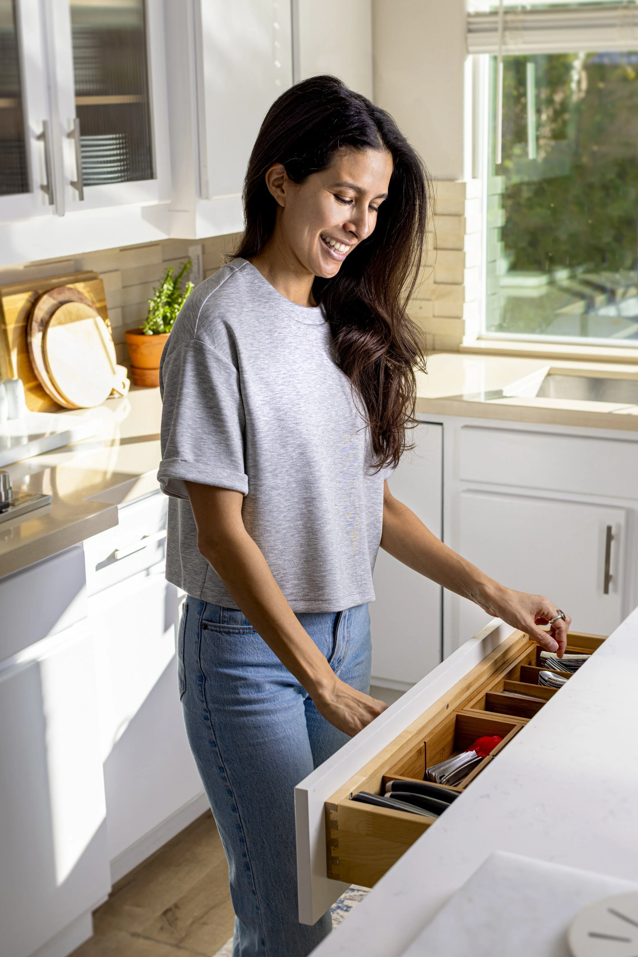 The founder of The Tidy Armadillo, Jessi, is opening a kitchen drawer with utensils in a modern kitchen.