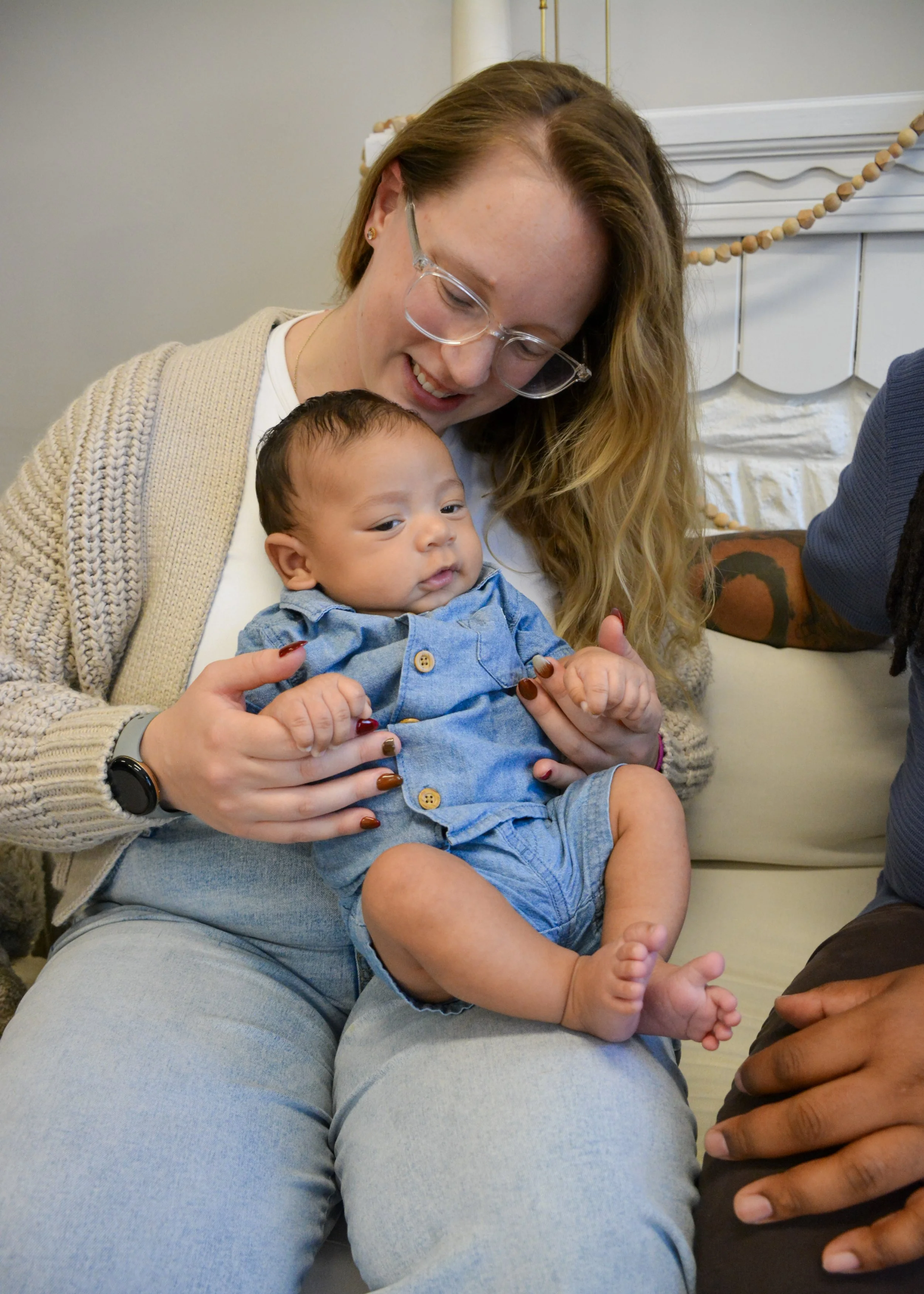 Woman holding a baby boy siting on her lap, smiling and looking down, indoors, with a decorated fireplace in the background.
