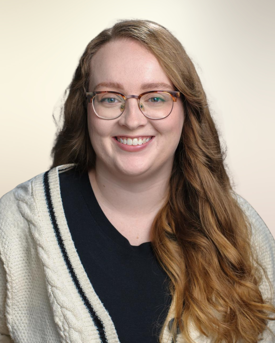 A woman with long wavy red hair, glasses, and a black shirt, smiling in front of a plain, light-colored background.