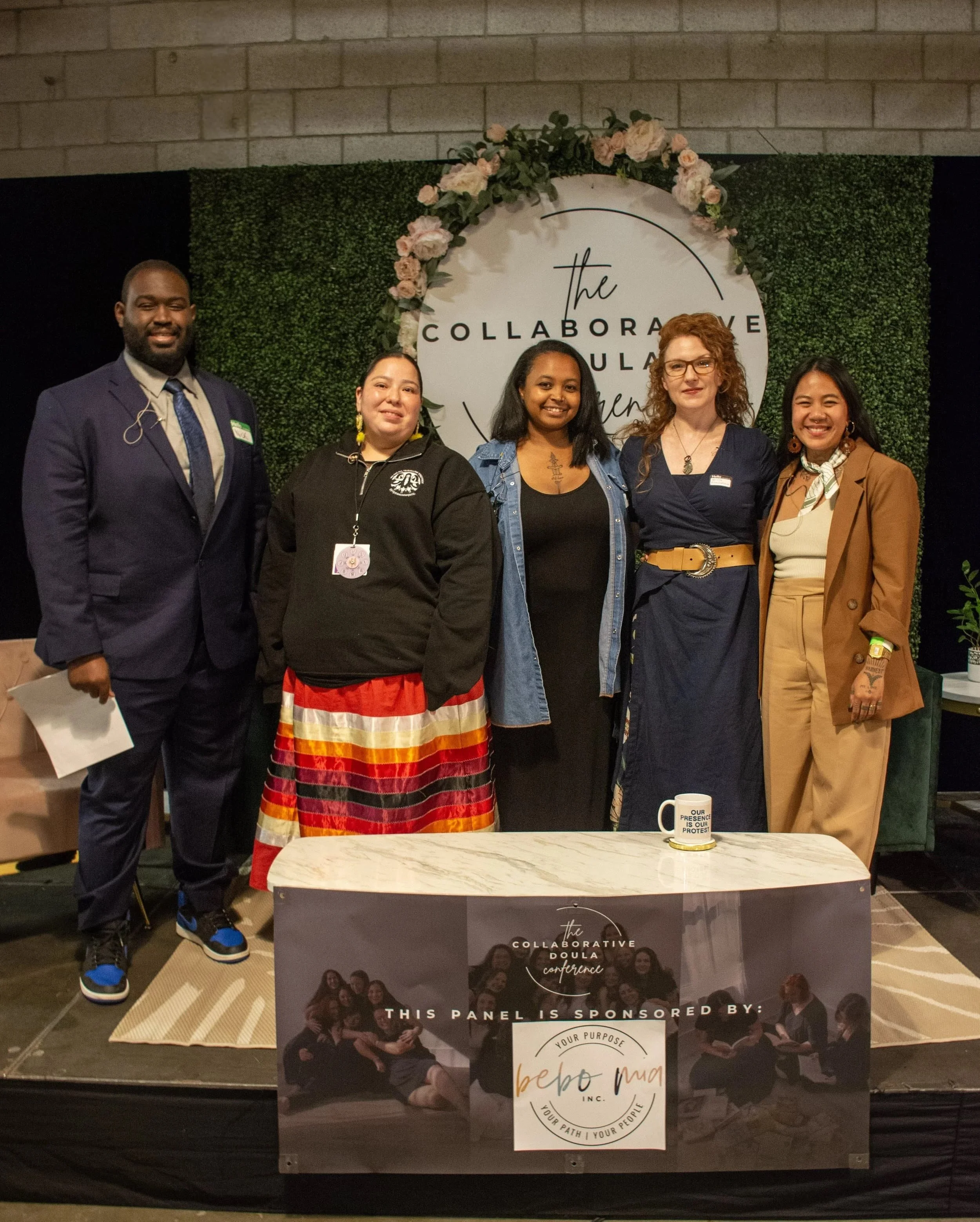 Group of five women and one man standing behind a table at The Collaborative Doula Conference in London, Ontario.