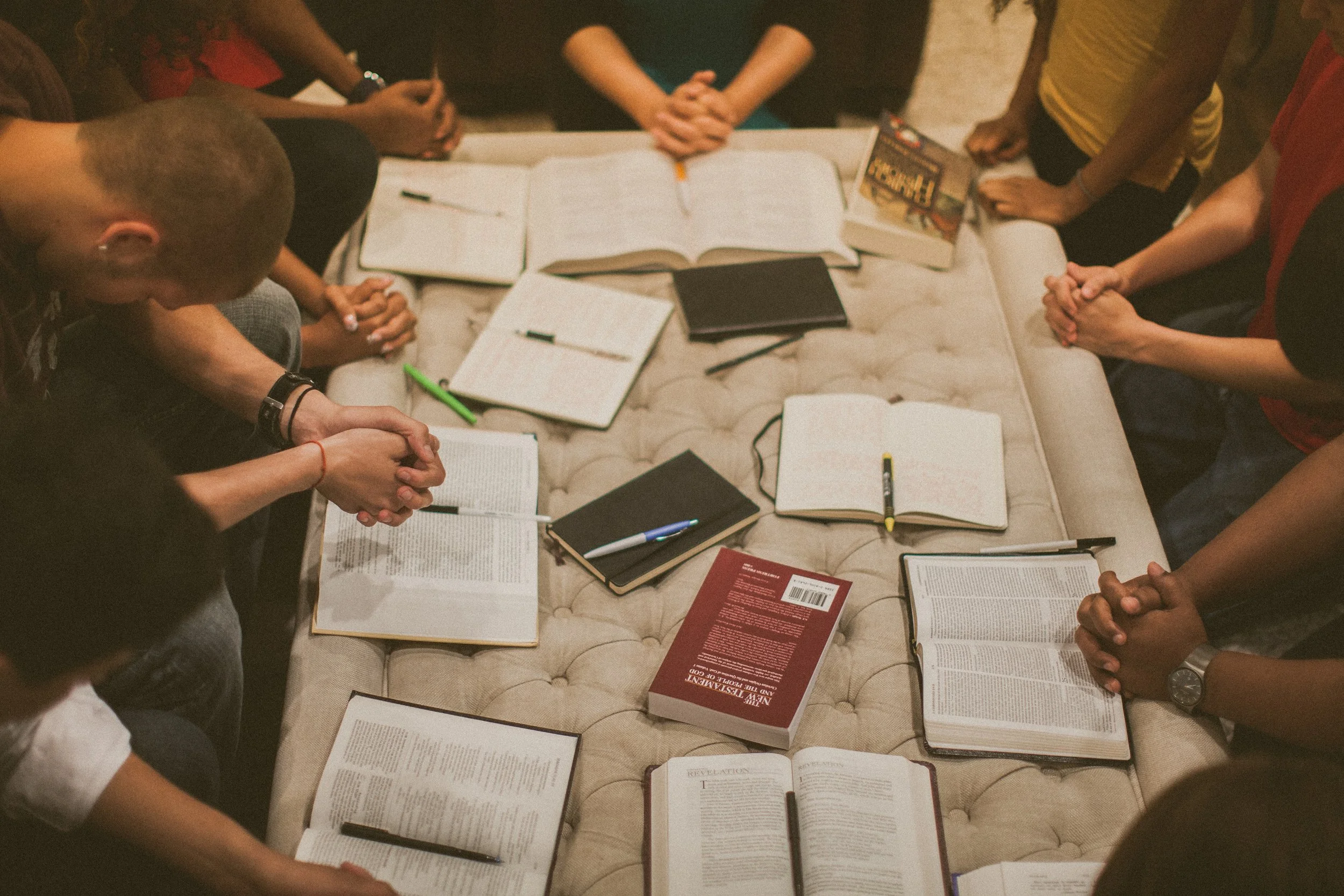 People are gathered around a table with open books, notebooks, pens, and highlighters, engaged in a discussion or study session.