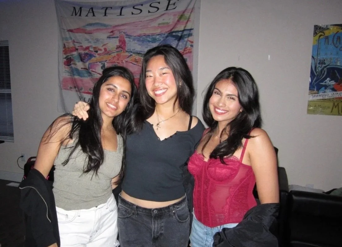 Three women posing together indoors, smiling, with a Matisse art print hanging on the wall behind them.