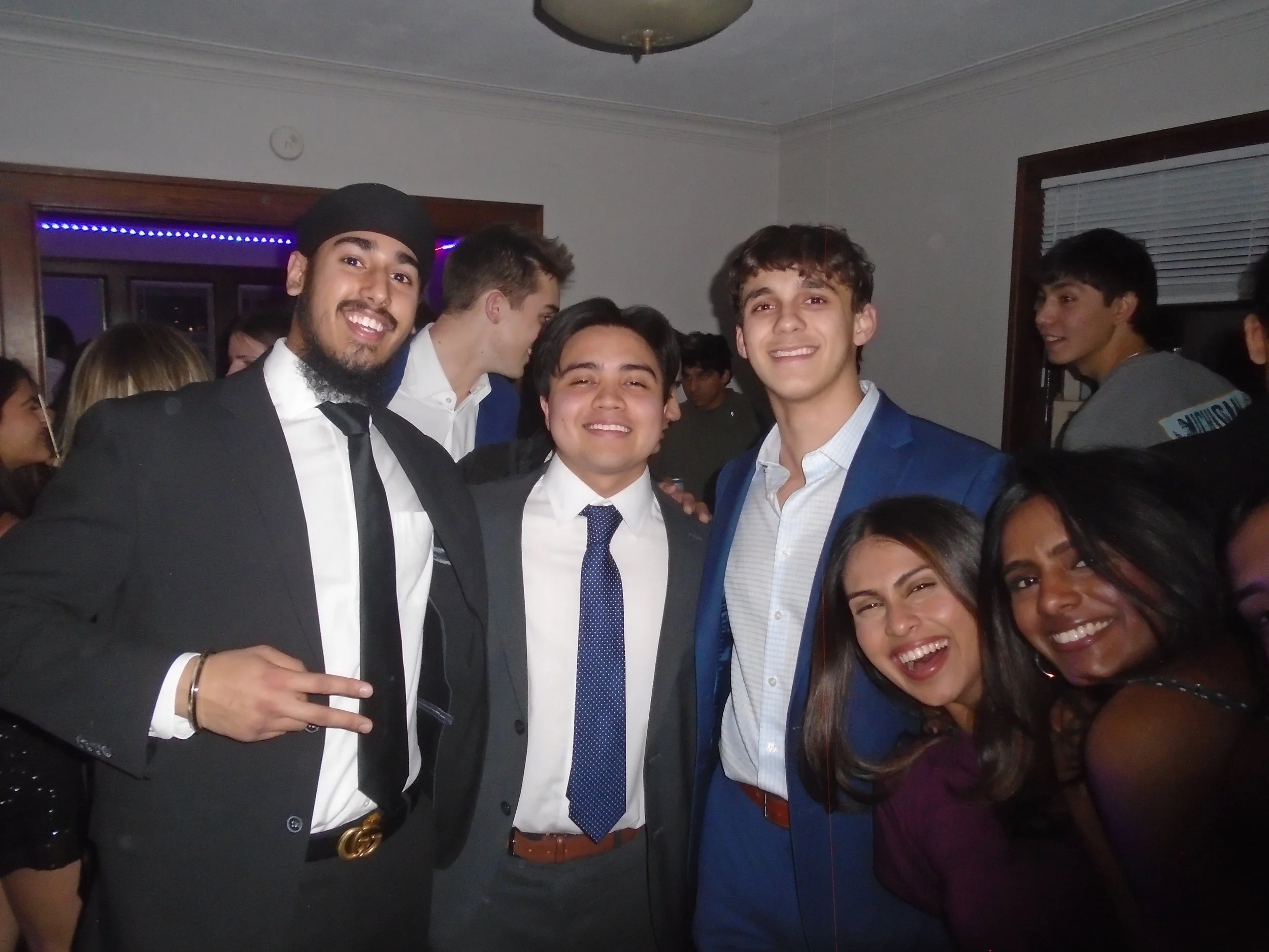 Group of young people smiling and posing for a photo at a party, dressed in formal and semi-formal attire.