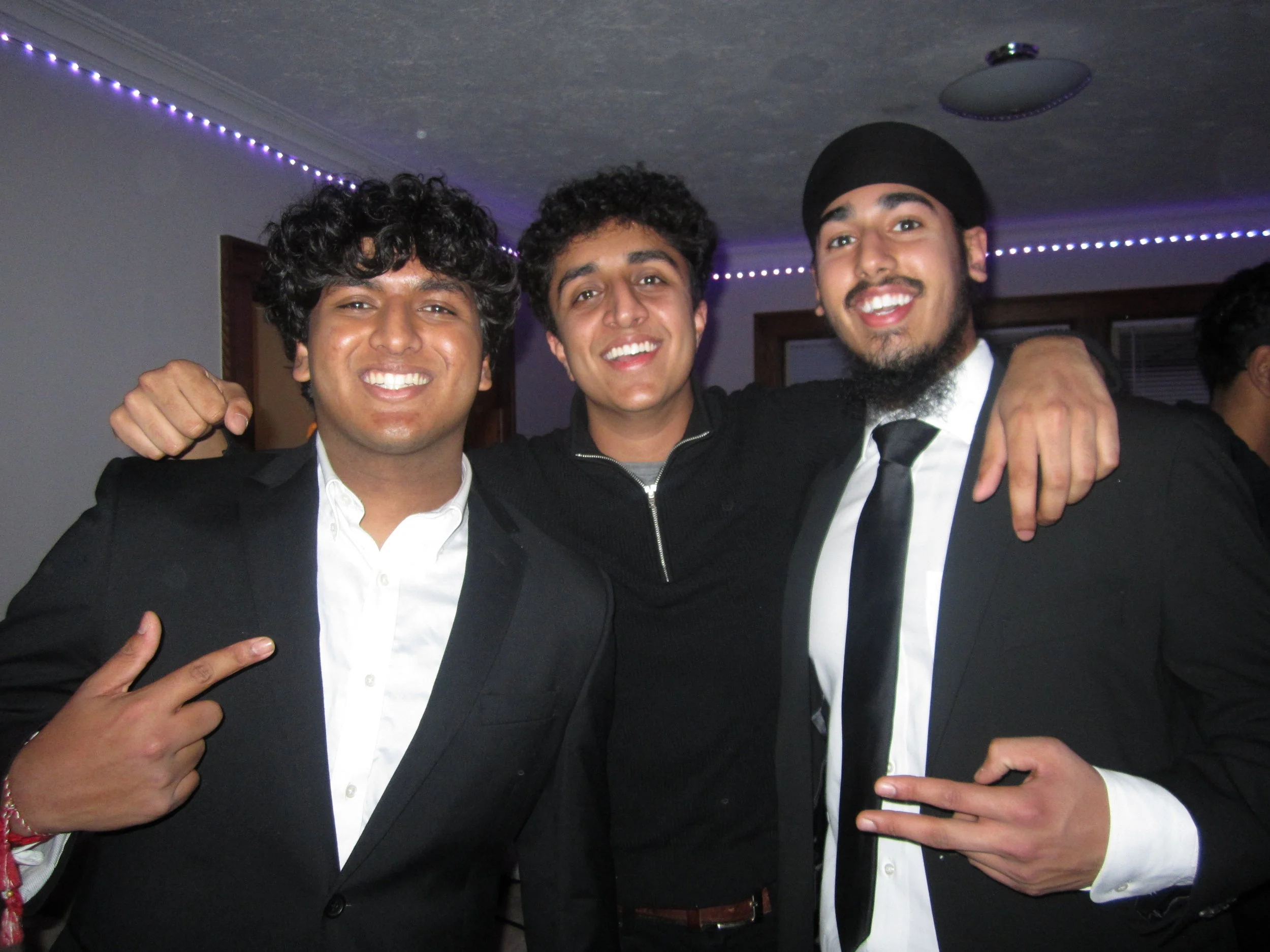 Three young men in formal attire smiling and posing together at a celebration or party.