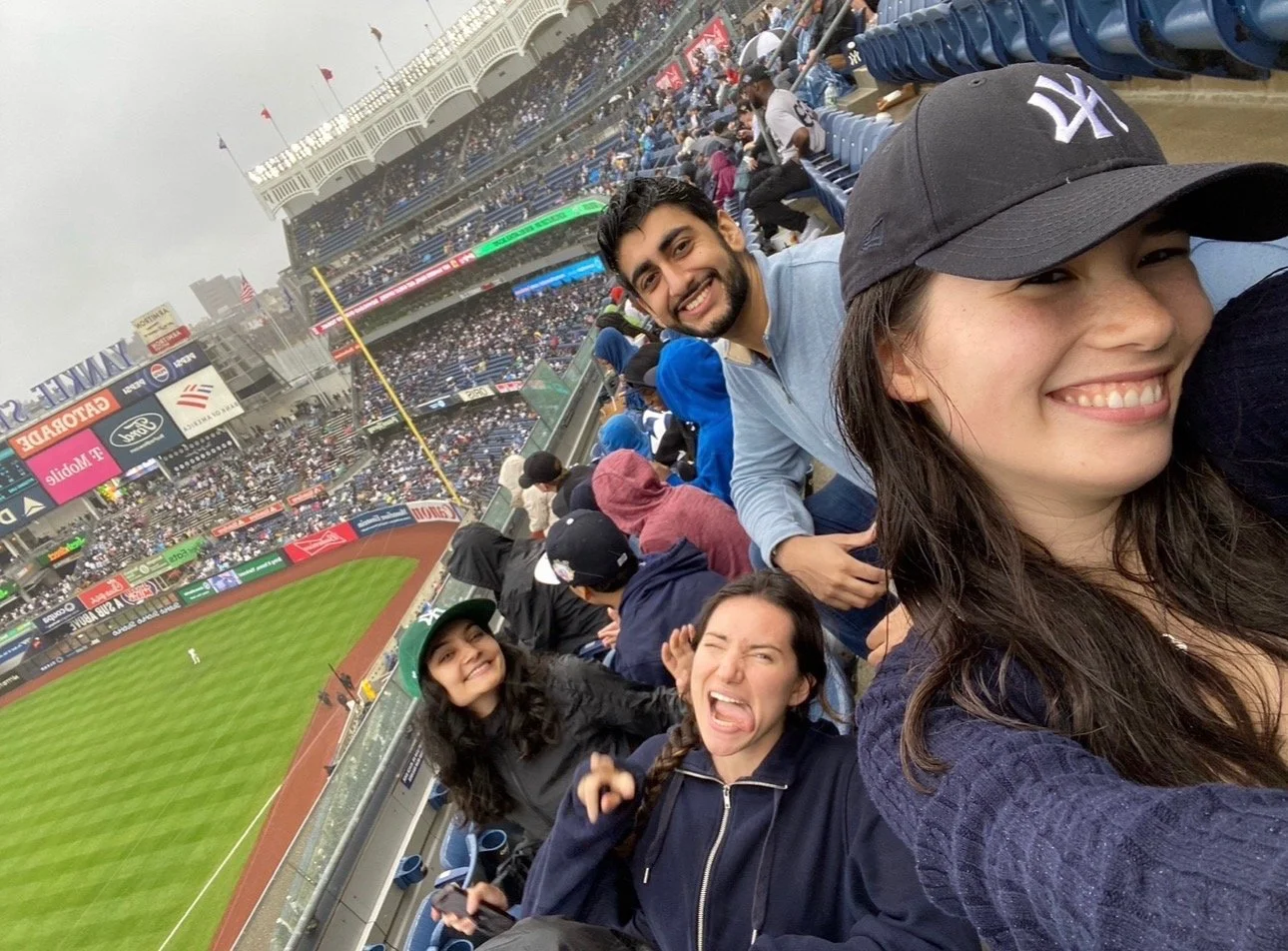 Smiling group of friends taking a selfie at a baseball game in a stadium filled with spectators.