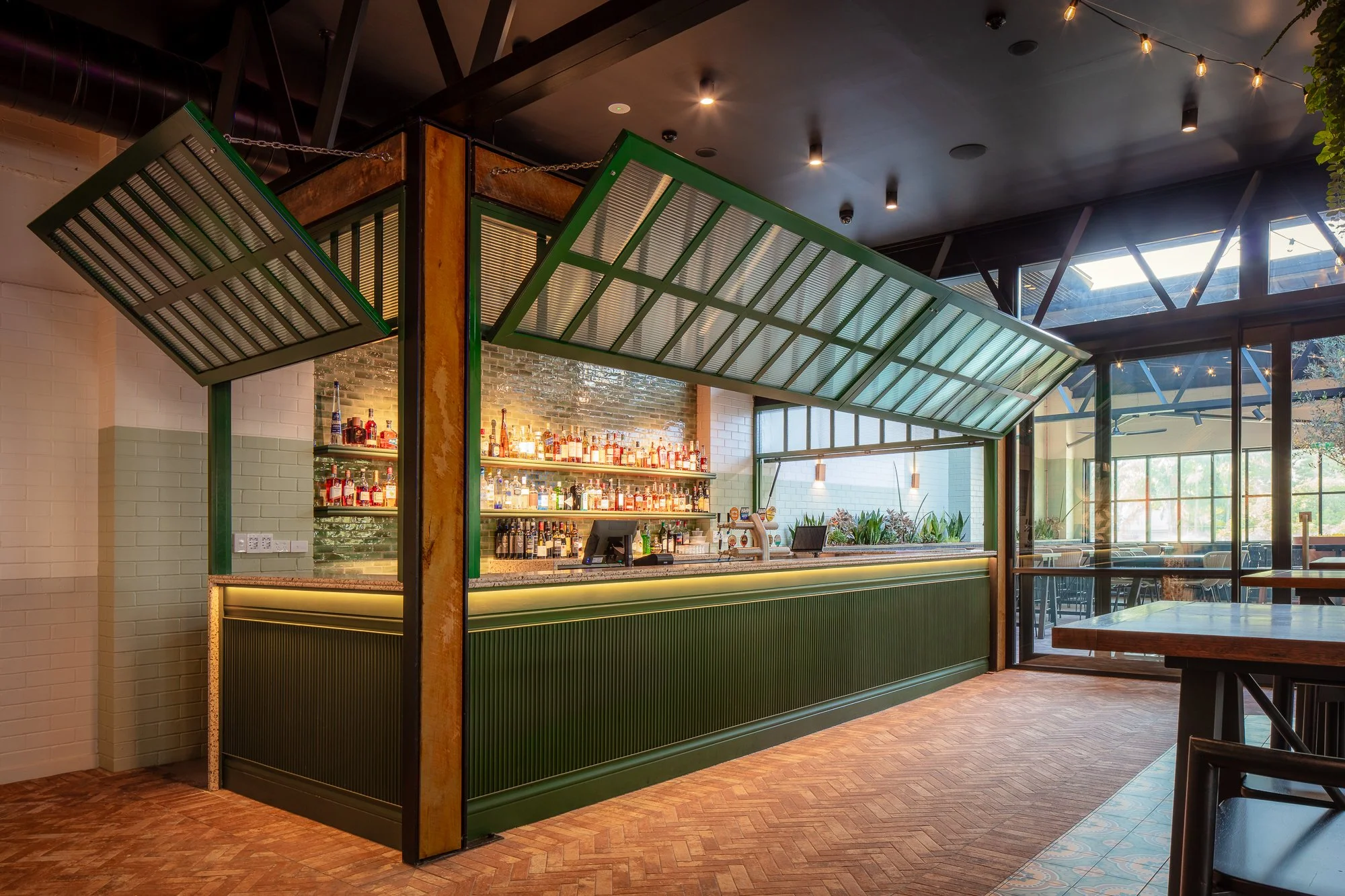 Zephyr Rooftop Bar Brisbane designed by Liife Architecture — green bar pavilion with canopy wings open, herringbone brick floor, courtyard beyond.