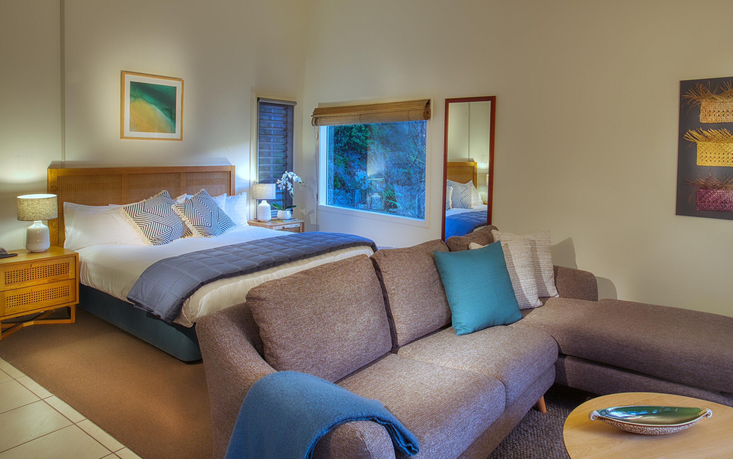 Cosy studio room with a bed, comfortable sofa, large window, and warm lighting in a relaxed setting.