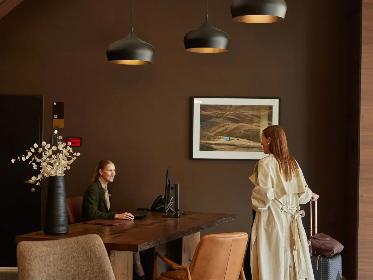 Luxury hotel reception check-in area with guest arriving at front desk and concierge assistance in a modern warm-toned lobby interior