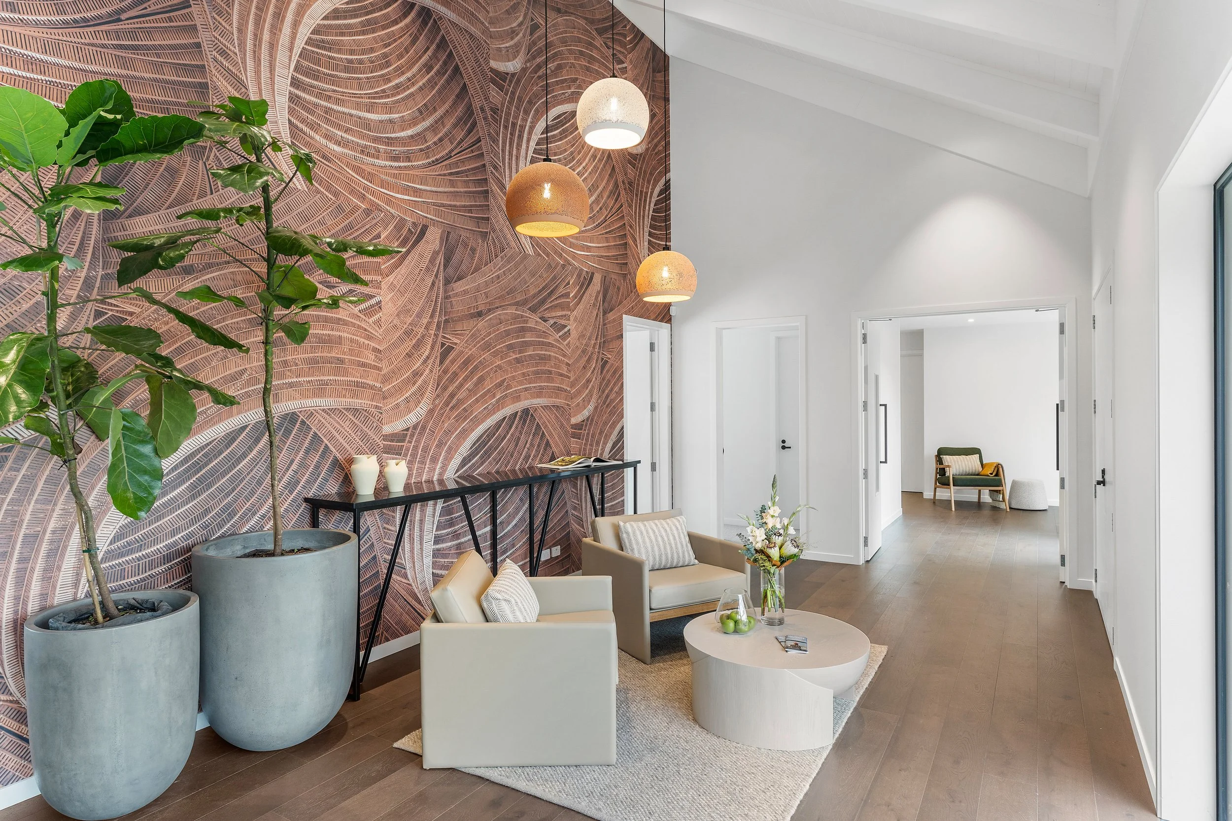 Stylish hotel lounge or lobby with modern armchairs, large indoor plants, abstract wood-textured feature wall, and warm pendant lighting.