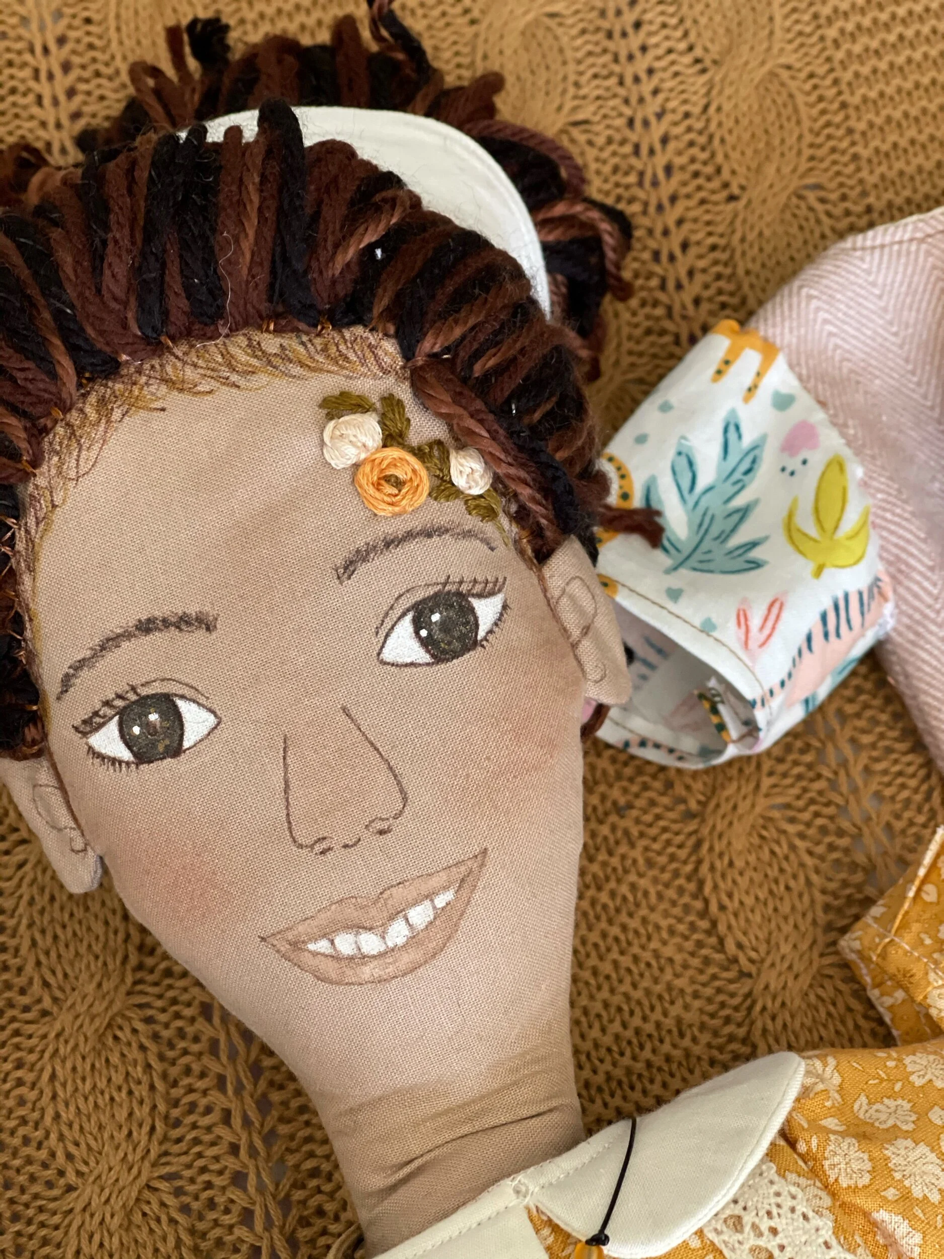 Handmade cloth doll with braided yarn hair and embroidered facial features, wearing a patterned dress.