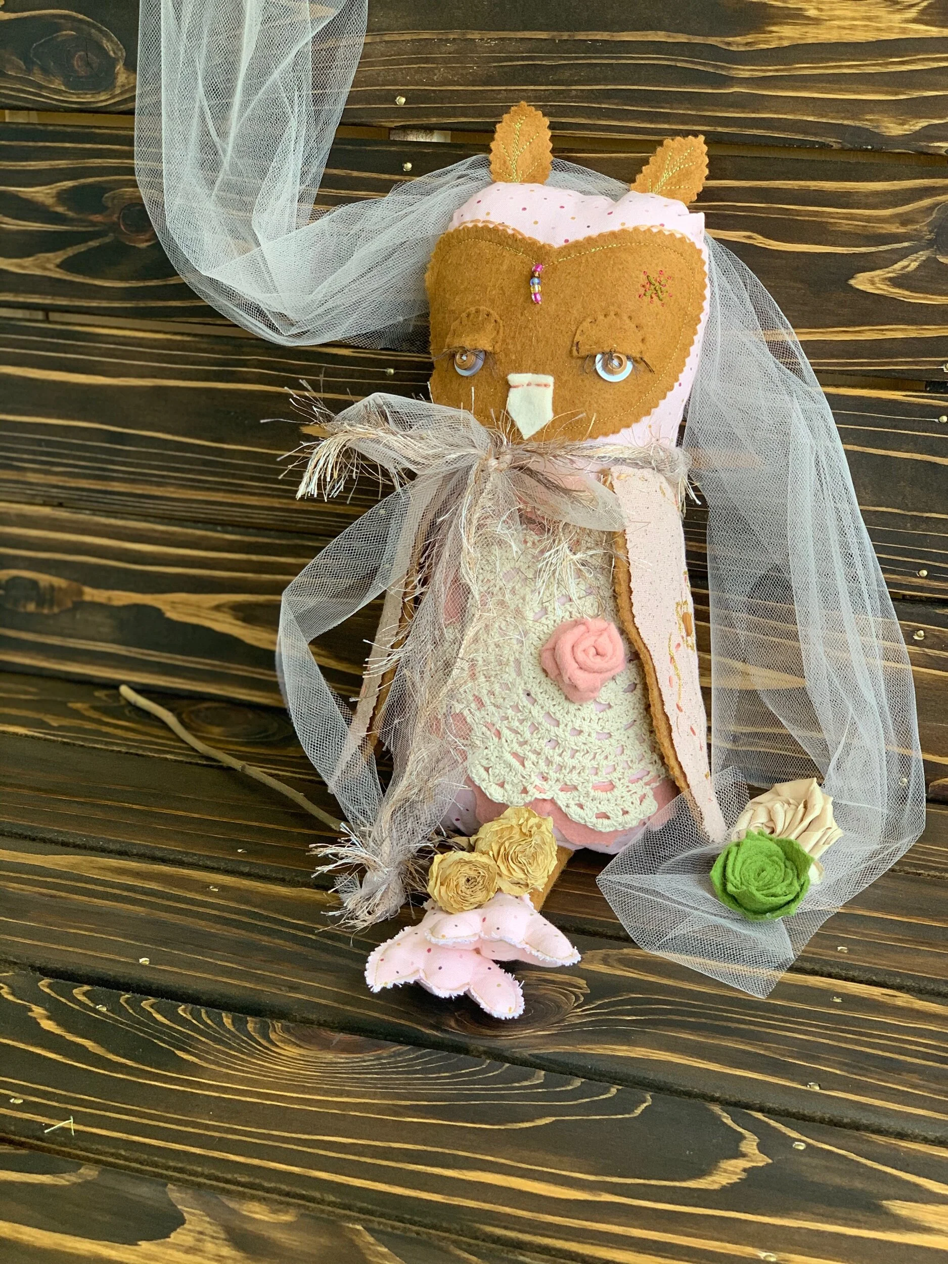 Stuffed owl doll with veil and floral decorations on wooden background.