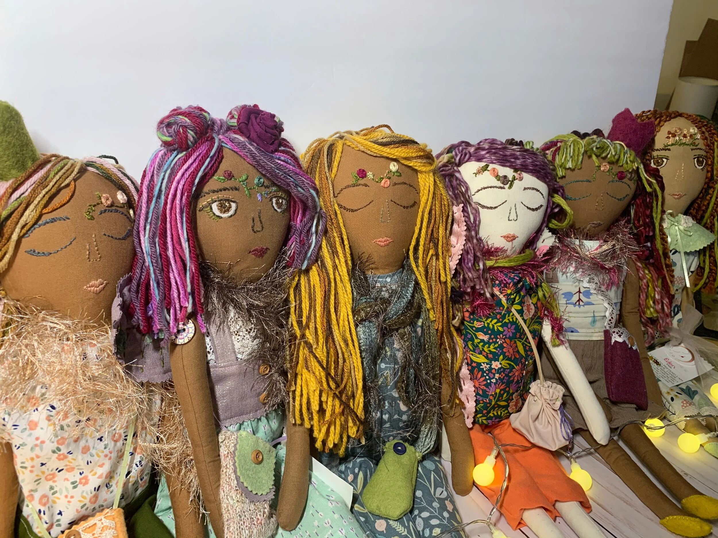 Handmade cloth dolls with embroidered and yarn hair, wearing colorful outfits, sitting in a row.