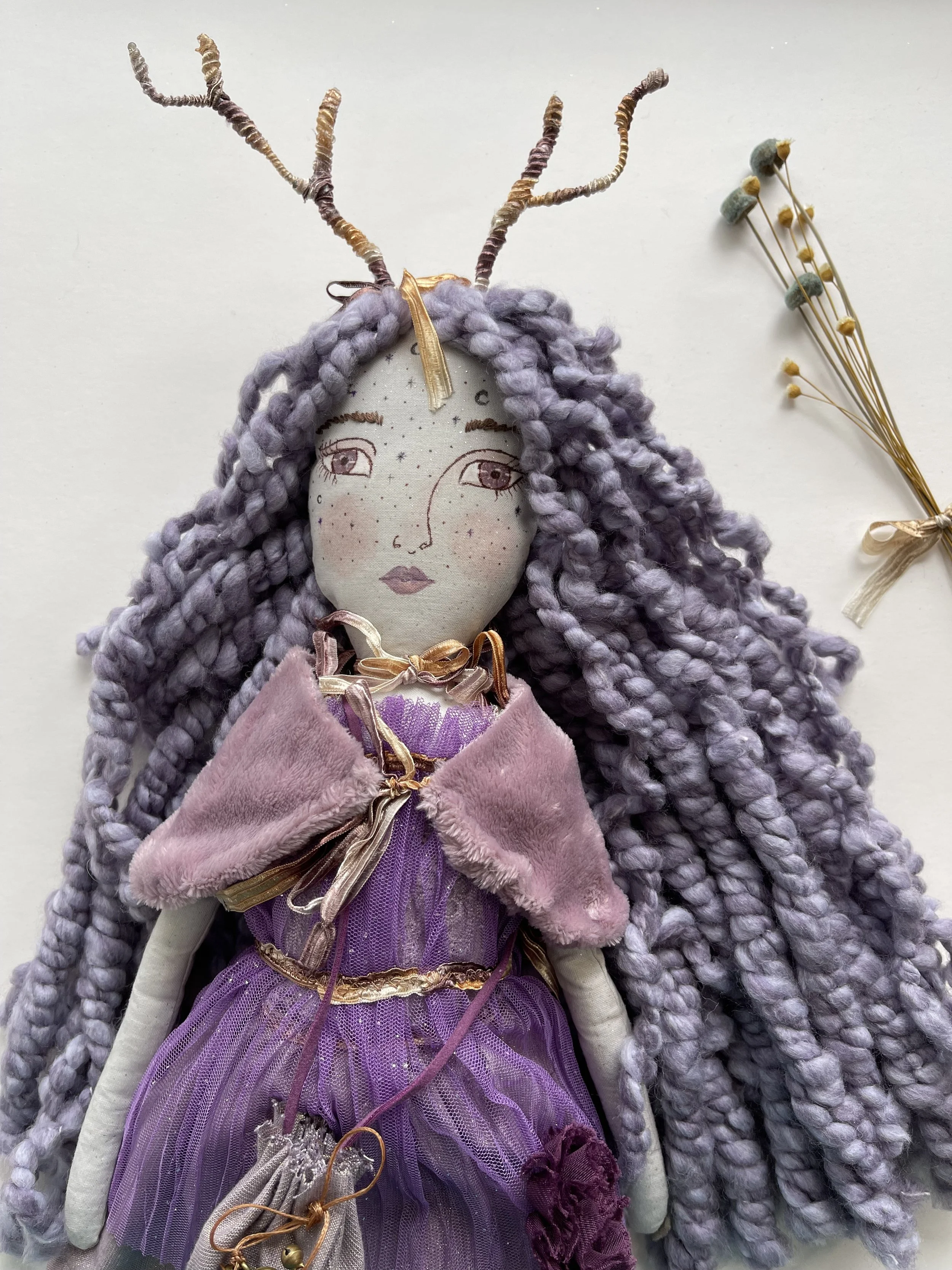 Handmade fairy doll with purple yarn hair, antler-like headpiece, purple dress, and decorative elements on a neutral background.