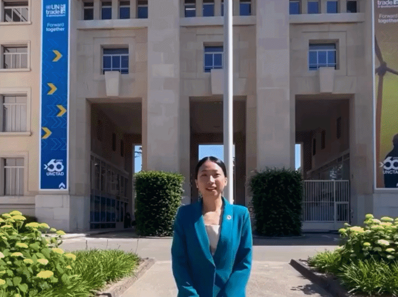 Woman in blue suit standing in front of United Nations building with banners on the side during the day.