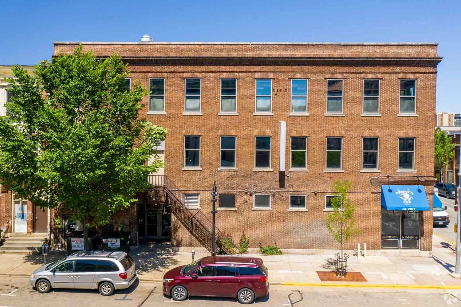 The Broom Street view of the red brick building with blue awnings at 320-328 West Gorham Street, Madison, WI 53703.