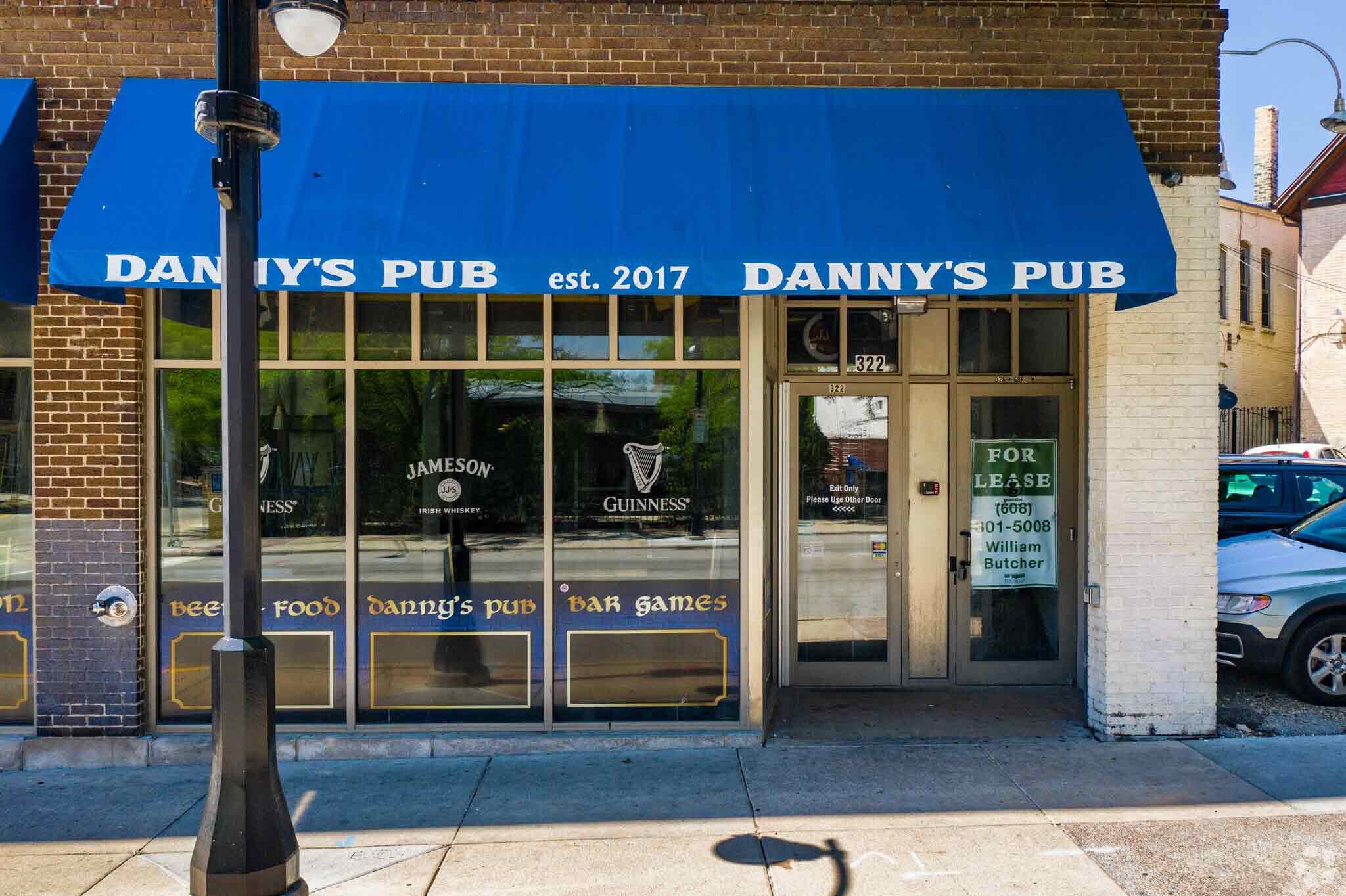 The storefront view of Danny’s Pub with  street level windows and blue awnings at 322 West Gorham Street, Madison, WI 53703.