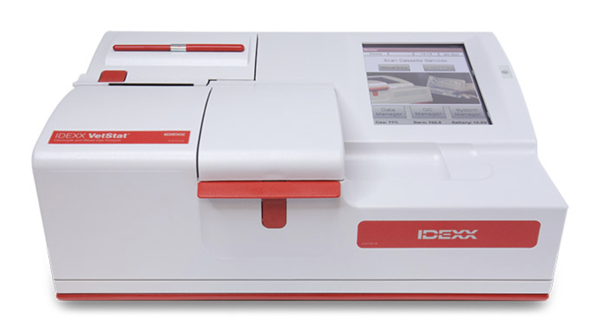 A laboratory blood analyzer machine, white with red accents, digital display screen, and a slot for testing samples.