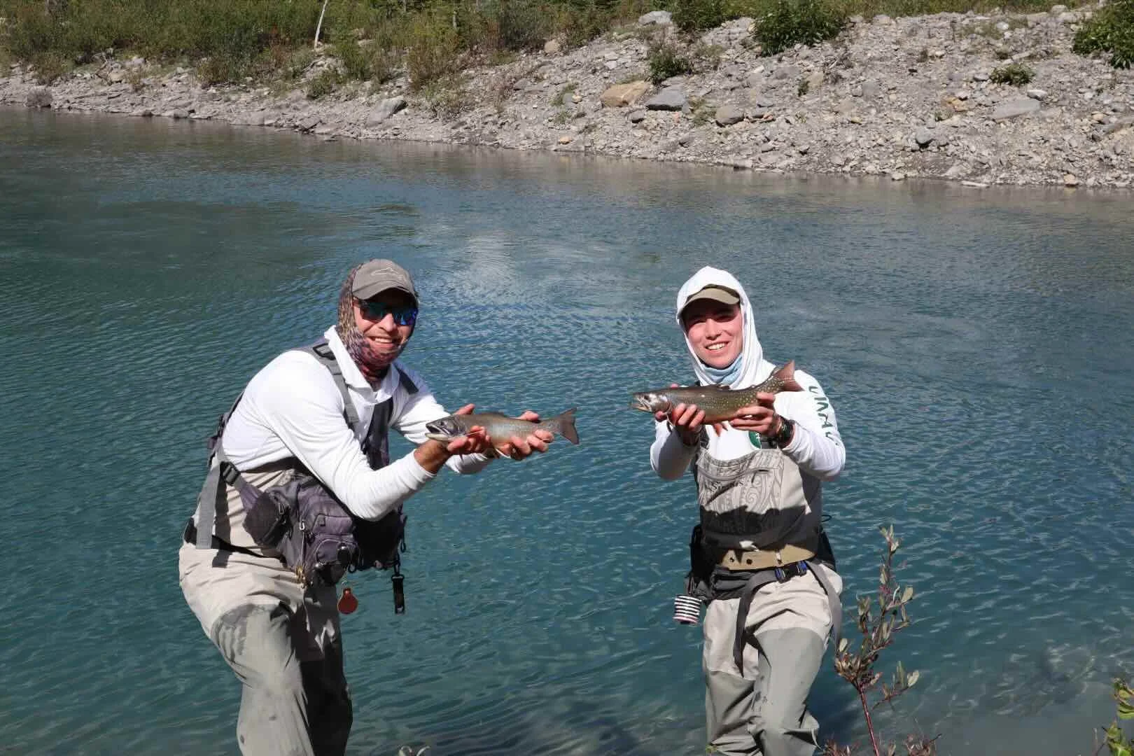 2 men holding huge brook trout in front of a lake