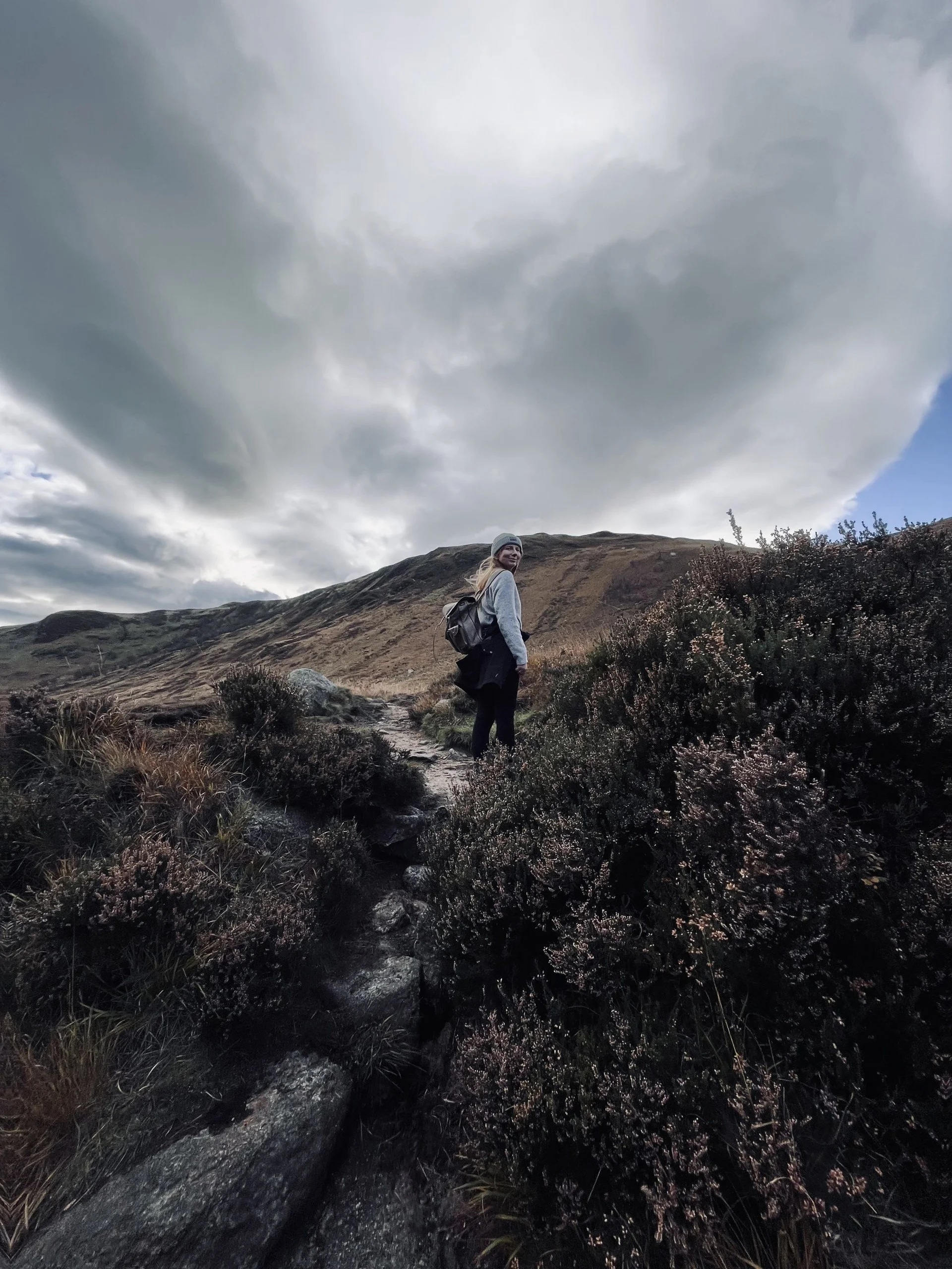 Rhona standing in Glen Rosa on the Isle of Arran in Scotland. A woman in her 30s standing among plants on a hillside on a cloudy autumn day.