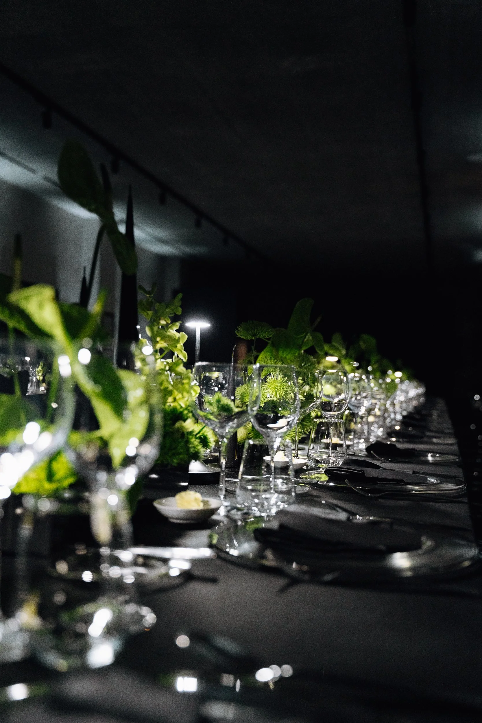 Elegant table setting at night with glassware, greenery, and dim lighting