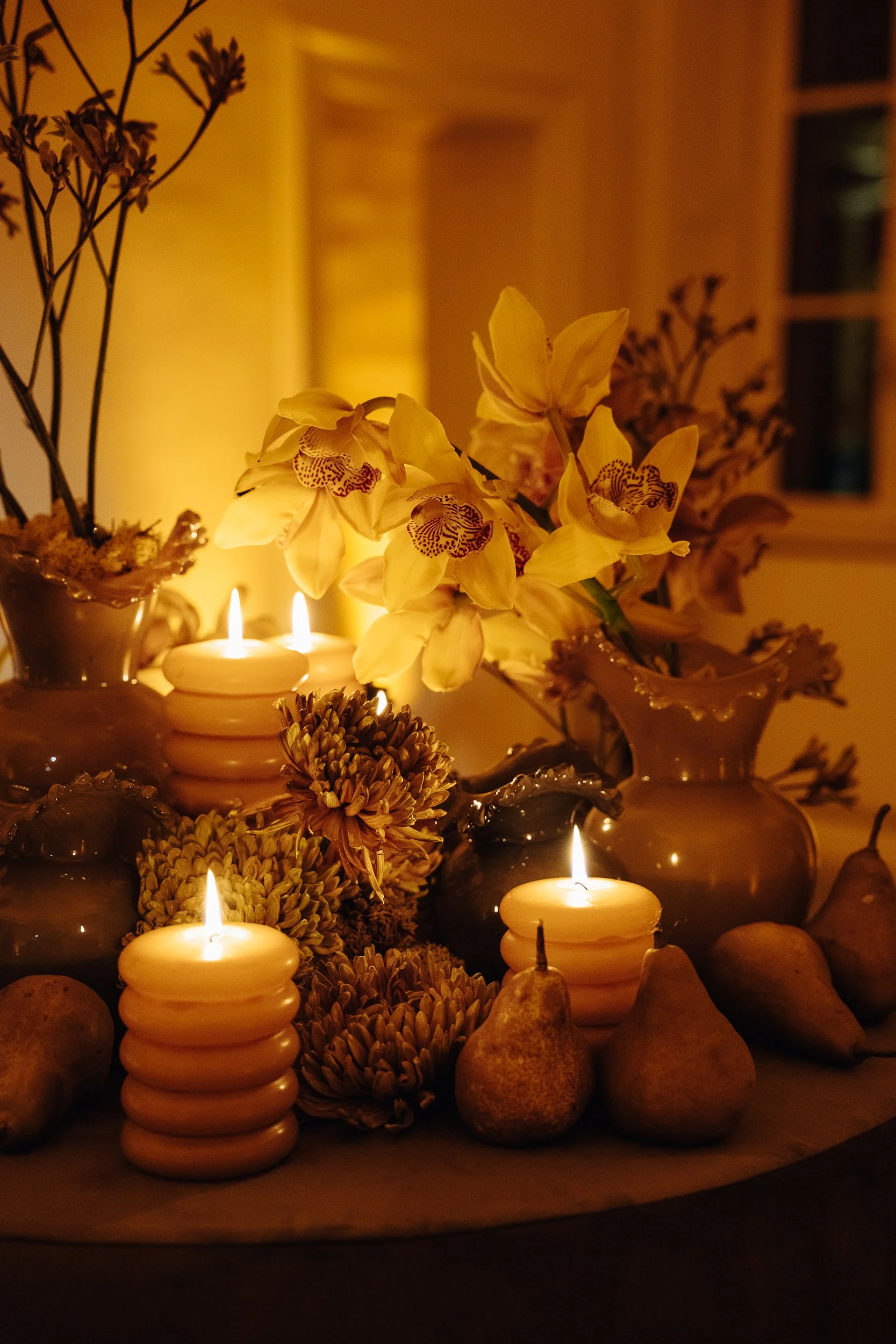 Decorative arrangement with yellow orchids, candles, rocks, and dried flowers illuminated softly in a warm indoor setting.