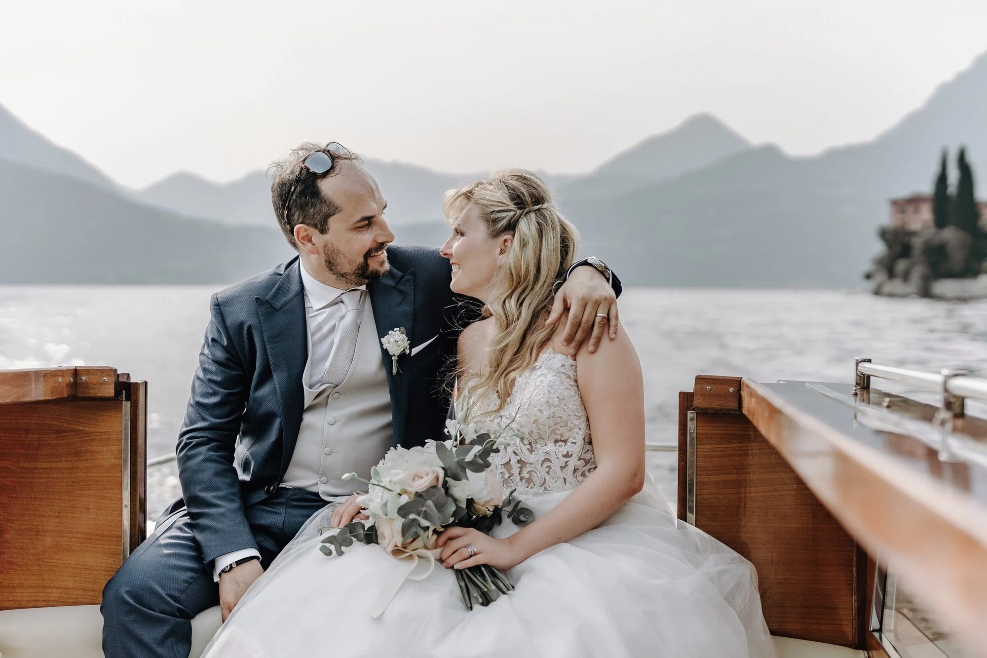 A newlywed couple sharing a romantic moment on a boat, with mountains and water in the background.