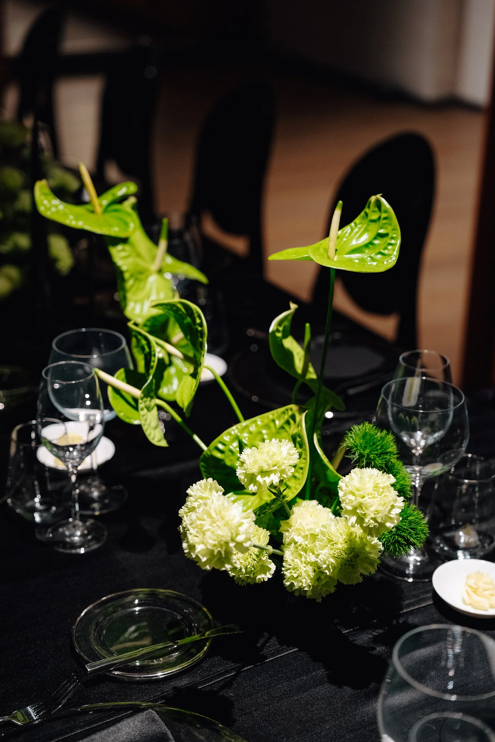 A floral centerpiece with green anthuriums and white carnations on a black table set for a formal event.