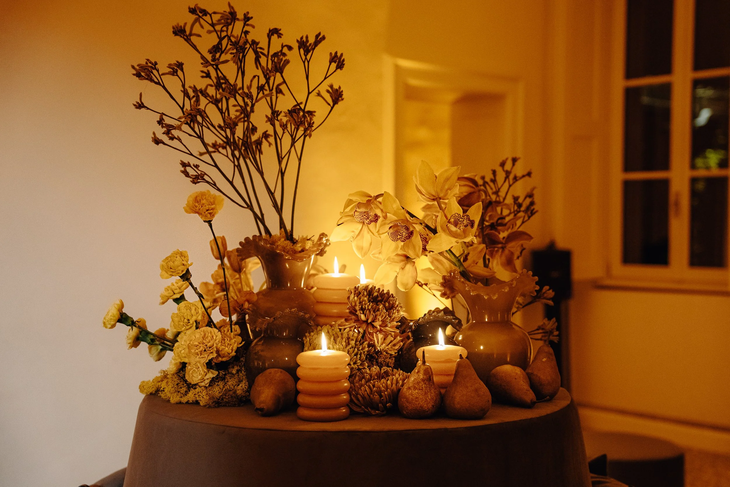 A table decorated with vases, candles, flowers, and rocks, softly illuminated in warm lighting.