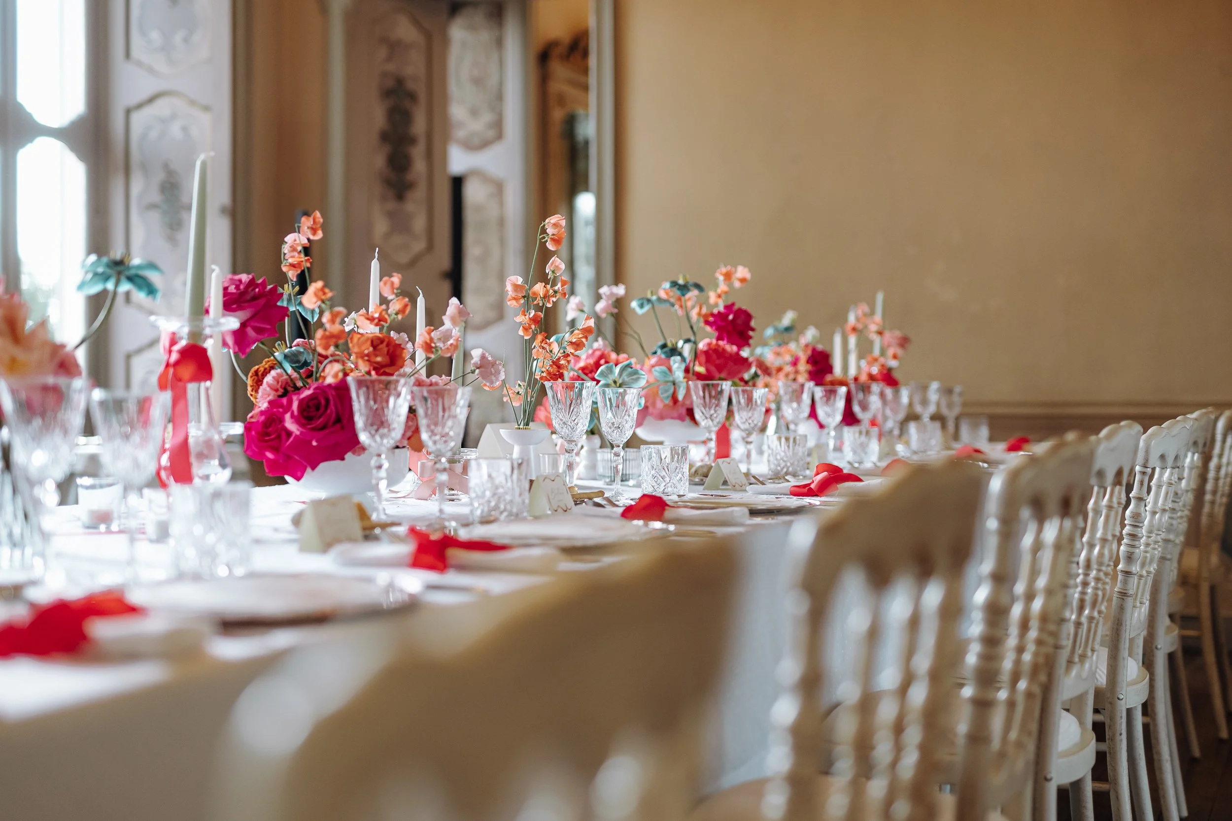 Elegant banquet table decorated with colorful flowers, candles, and glassware in a brightly lit, ornately decorated room.