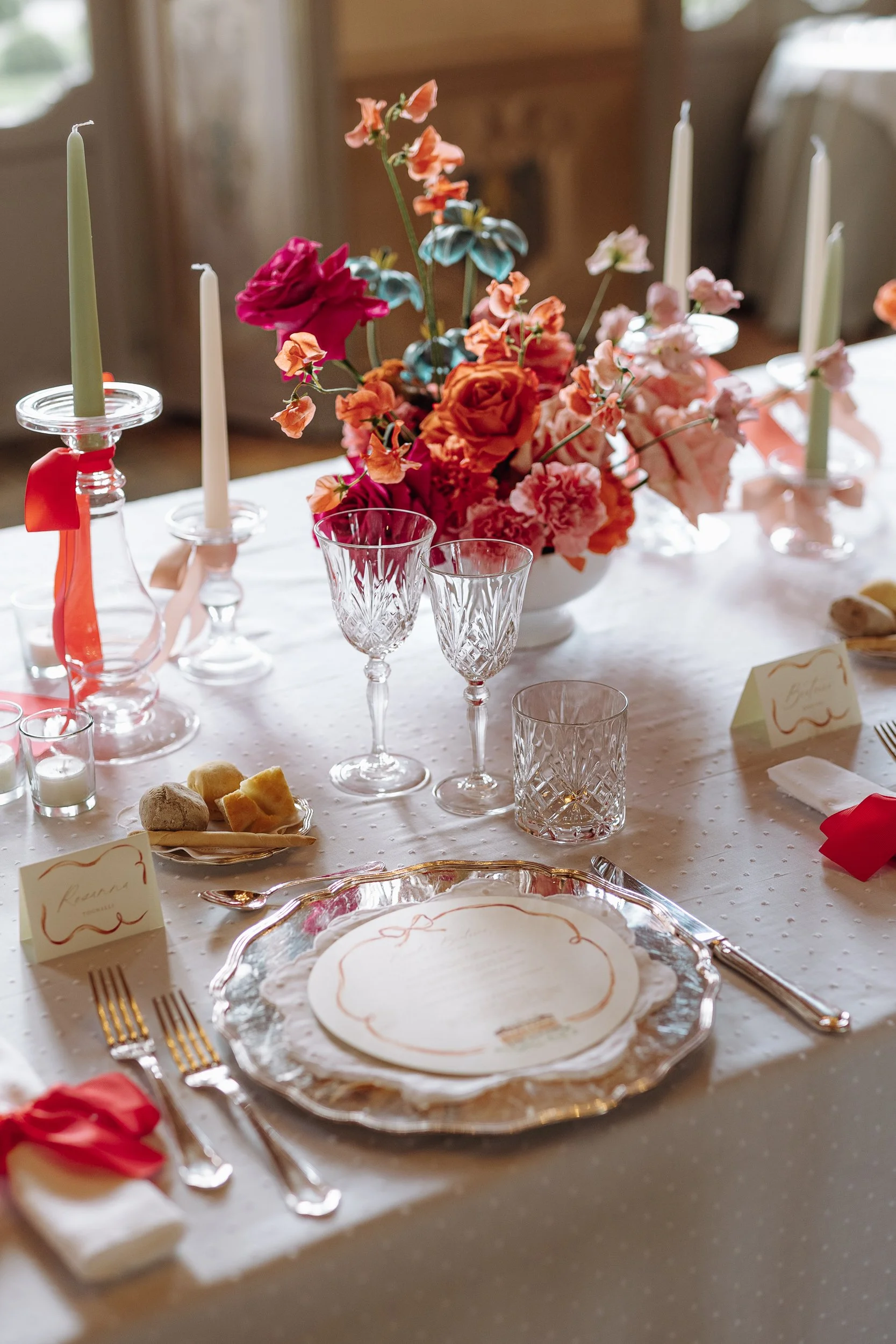 A table decorated for a special occasion with a floral centerpiece, crystal glasses, candles, and elegant tableware, set in a cozy room with soft lighting.