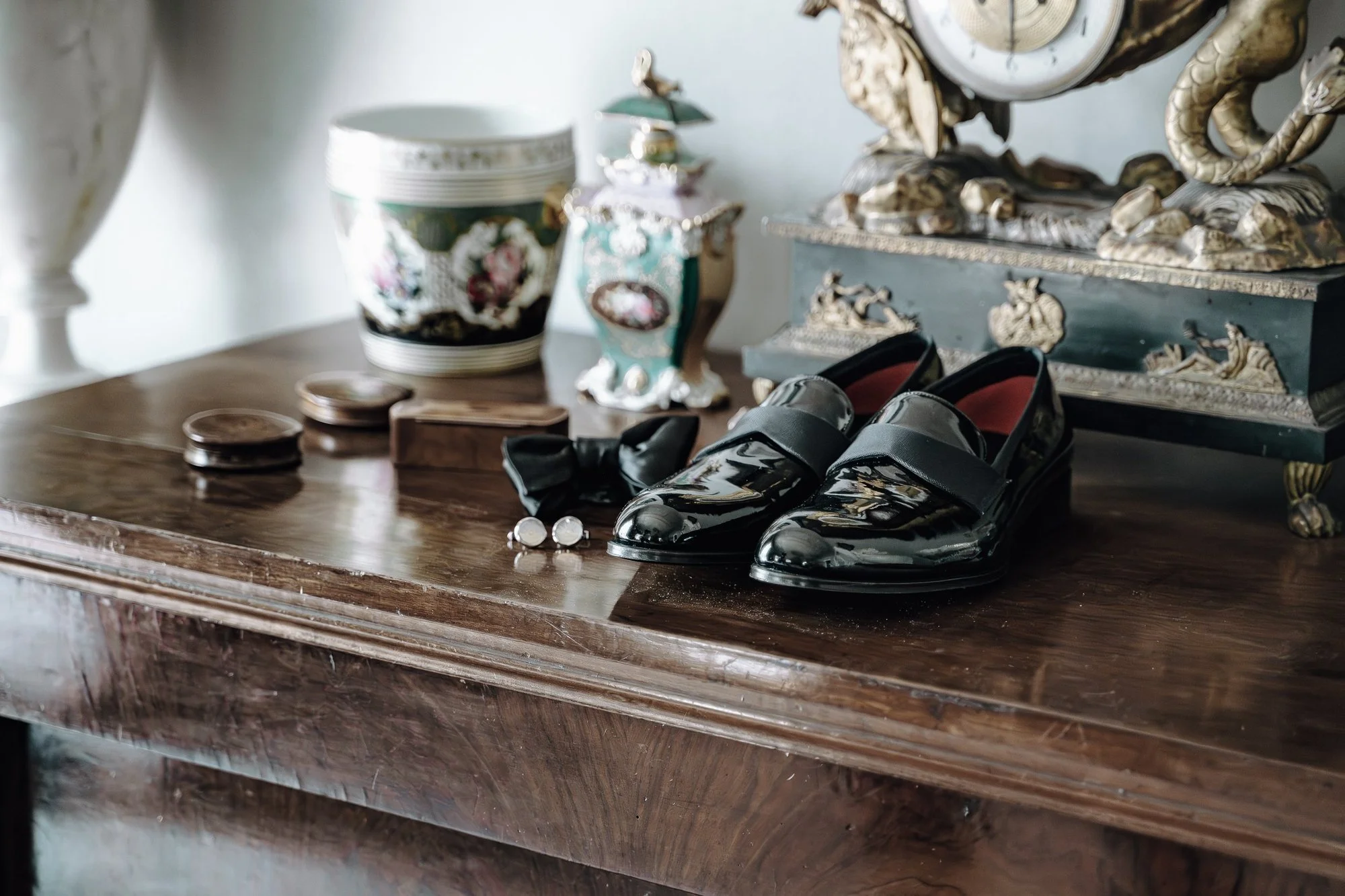 A wooden table with vintage shoes, jewelry, and decorative glassware, featuring ornate vases and a clock in the background.