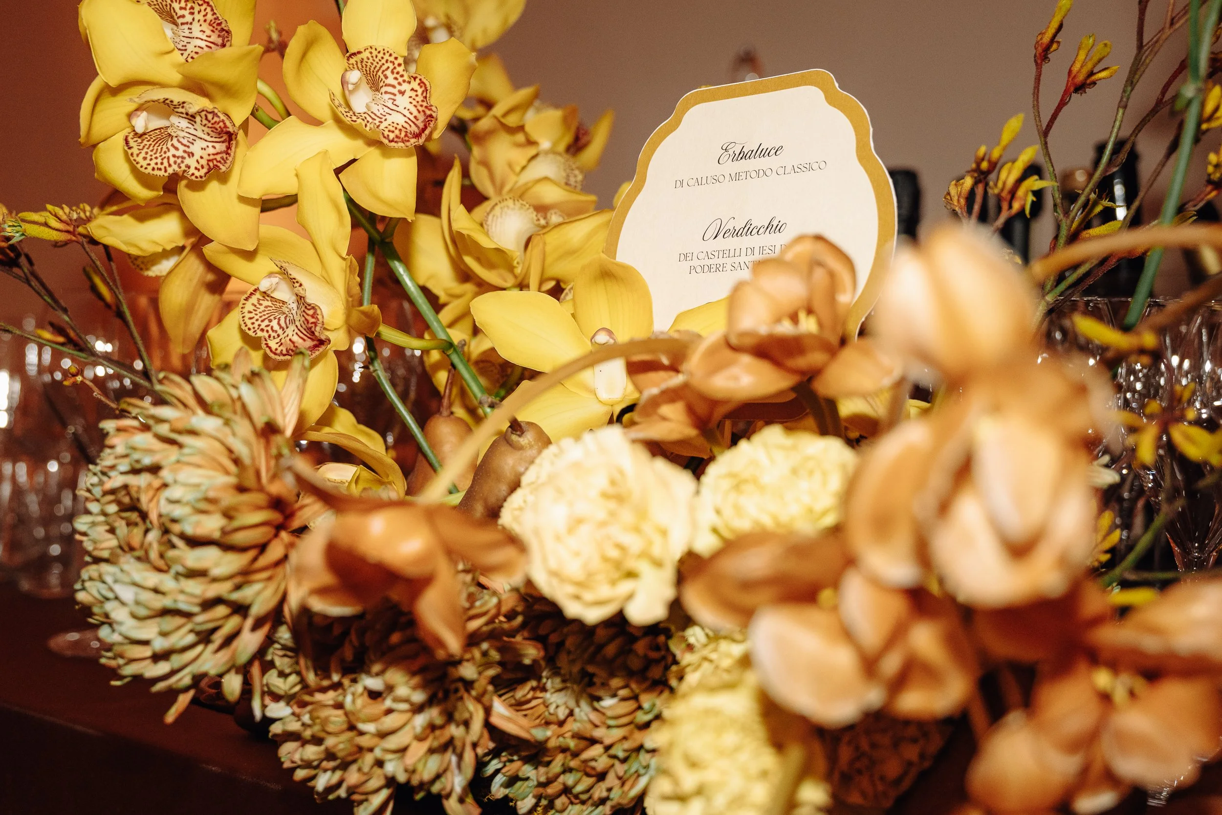 A bouquet of yellow orchids with a sign that reads 'Erbaluce di Caluso Metodo Classico Verdicchio dei Castelli di Jesi Podere Santo'