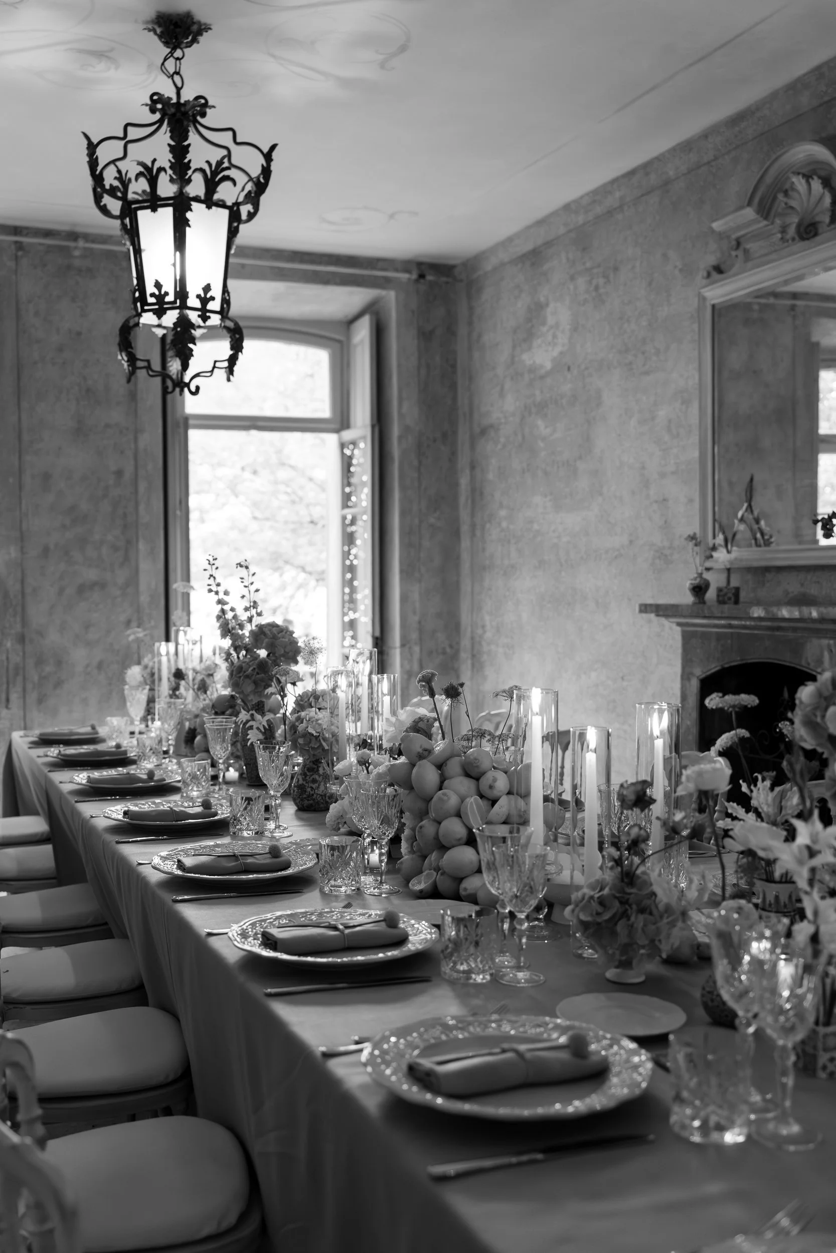 Elegant indoor dining room set up for a special event with a long rectangular table, floral centerpieces, and place settings on a tablecloth, with a vintage chandelier hanging from the ceiling.