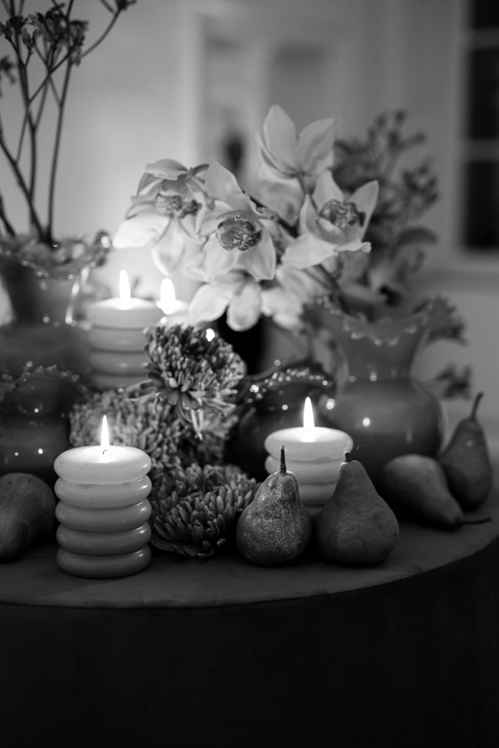 Black and white image of a floral arrangement with candles, pears, and other decorative objects.