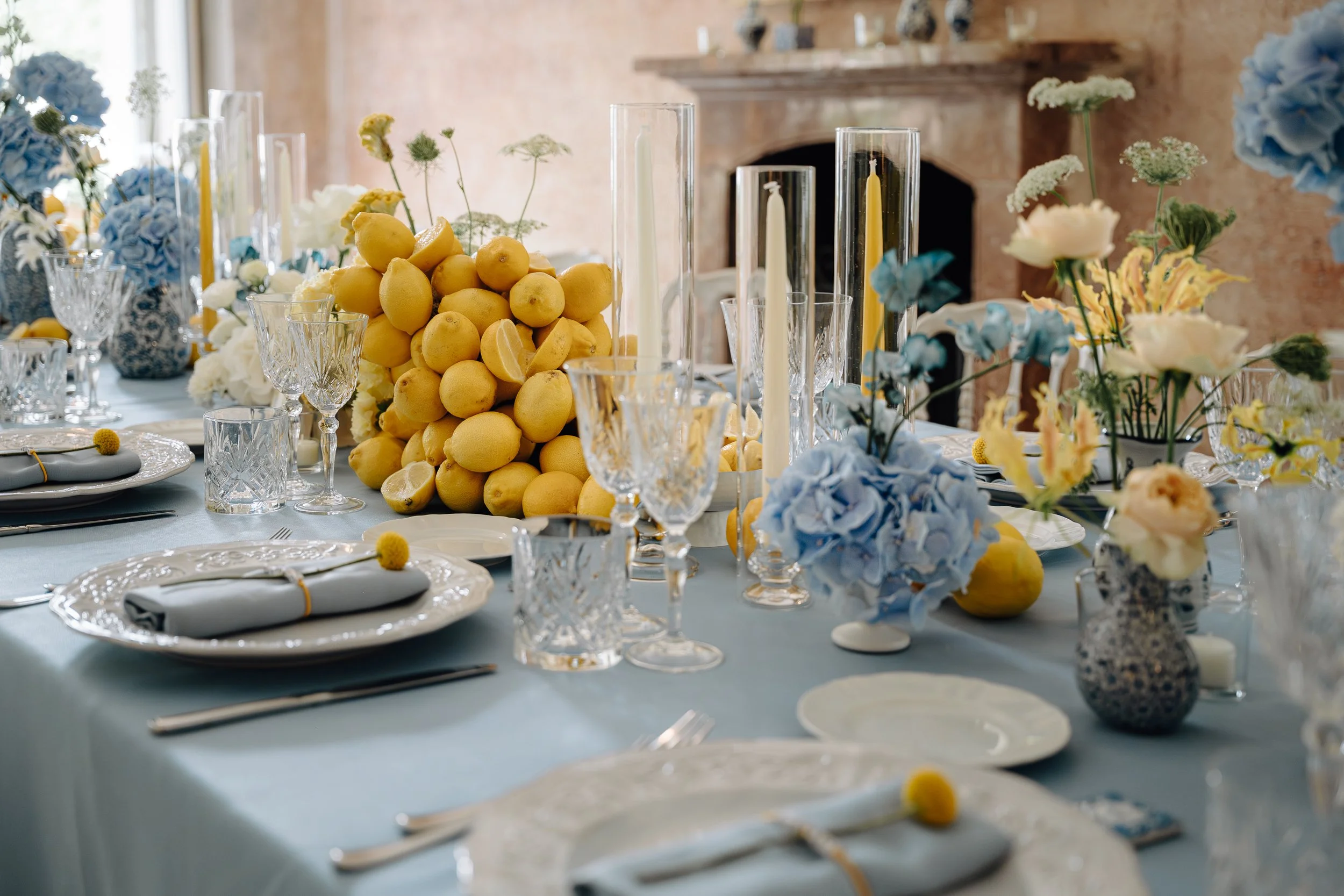 A table decorated with lemons, white and blue flowers, candles, and crystal glassware for a celebration or event.
