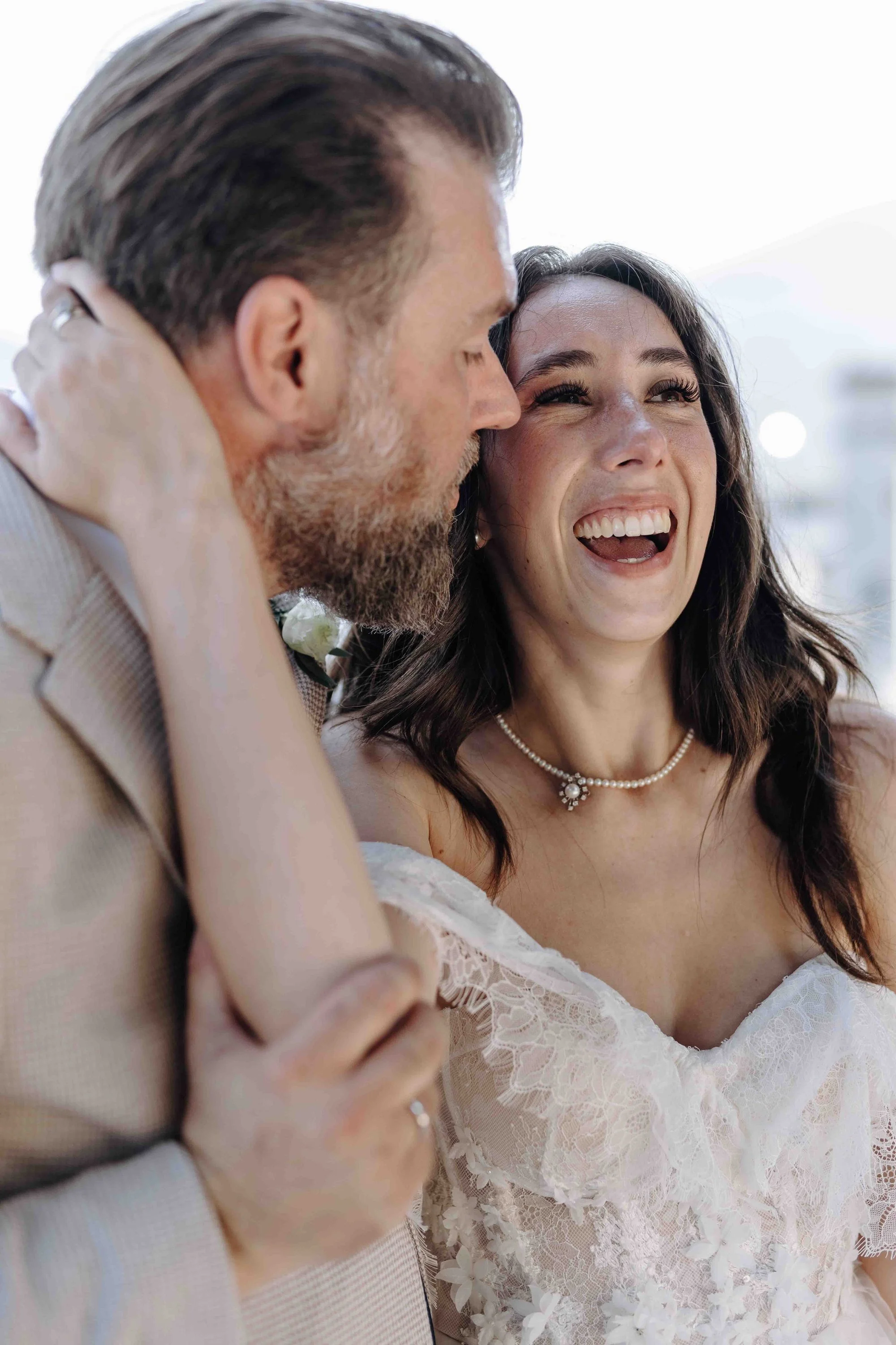 A couple dressed in wedding attire, smiling and closely embracing each other outdoors during daytime.