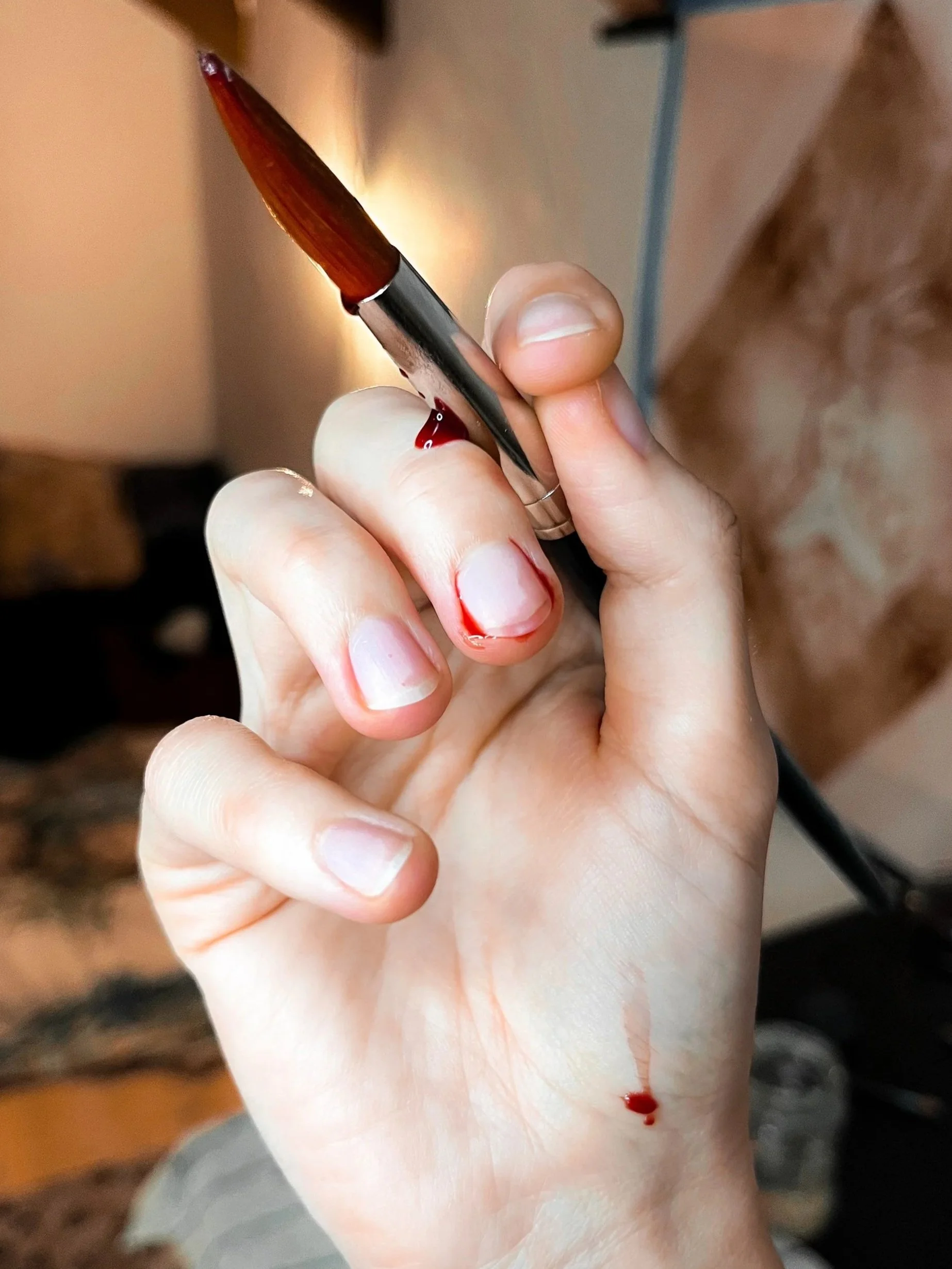 A person's hand holding a pen with period blood on the index finger and a small bloodstain on the hand.

Die Hand einer Person, die einen Pinsel in der Hand hält, Periodenblut am Mittelfinger und einen kleinen Tropfen an der Hand.