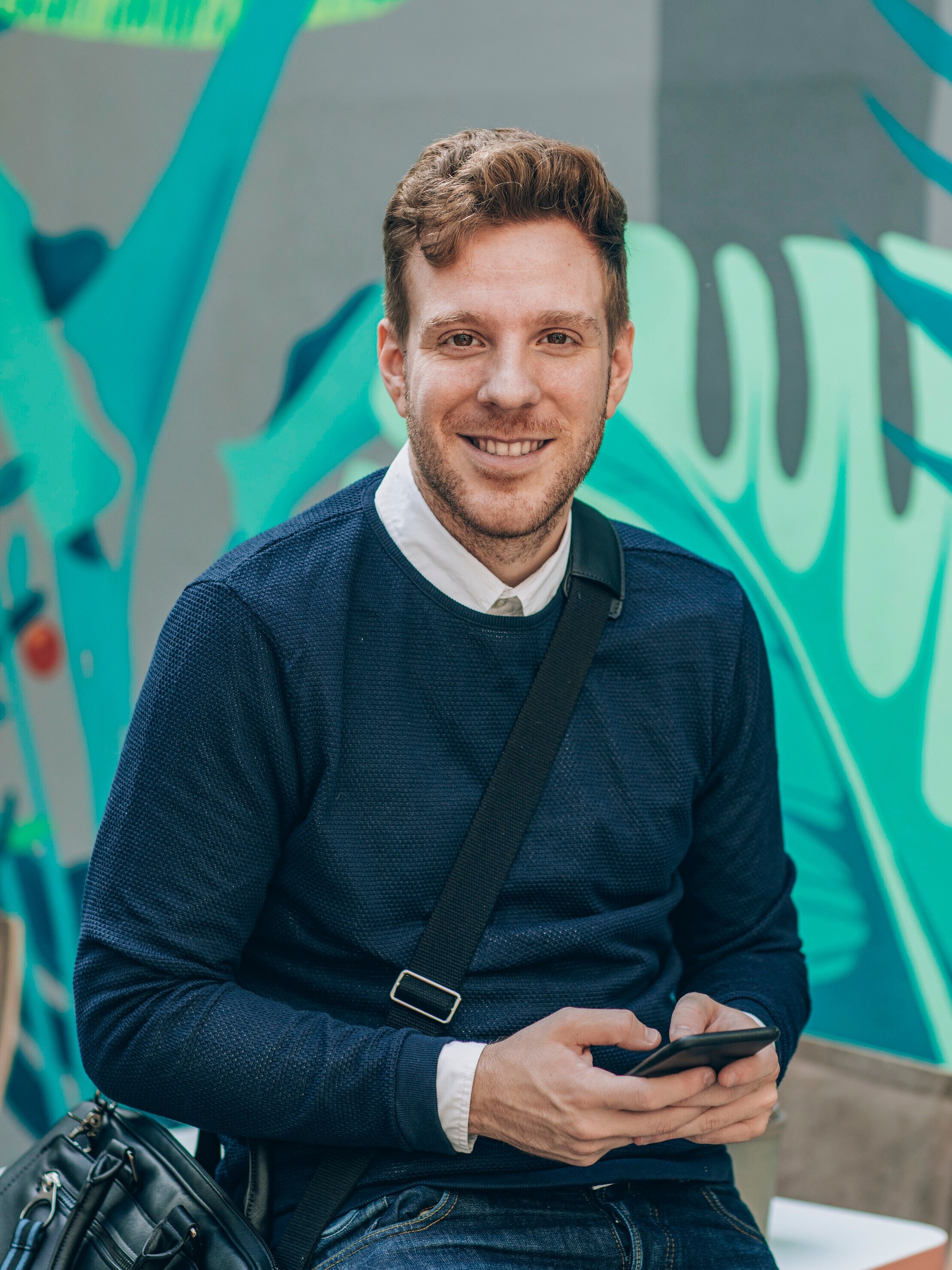 Portrait of handsome young smiling therapist holding smartphone and looking at camera.