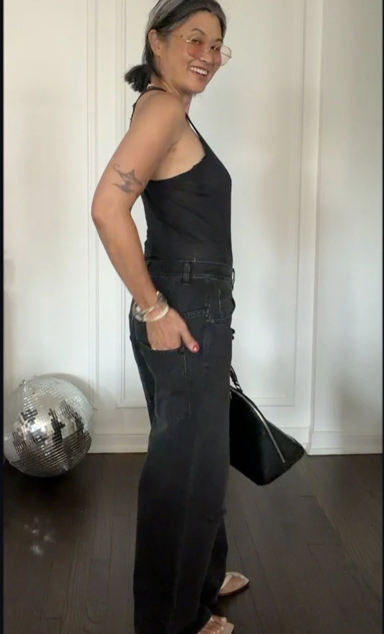 Woman over 50 wearing an all-black summer outfit with black denim and a black tank top.