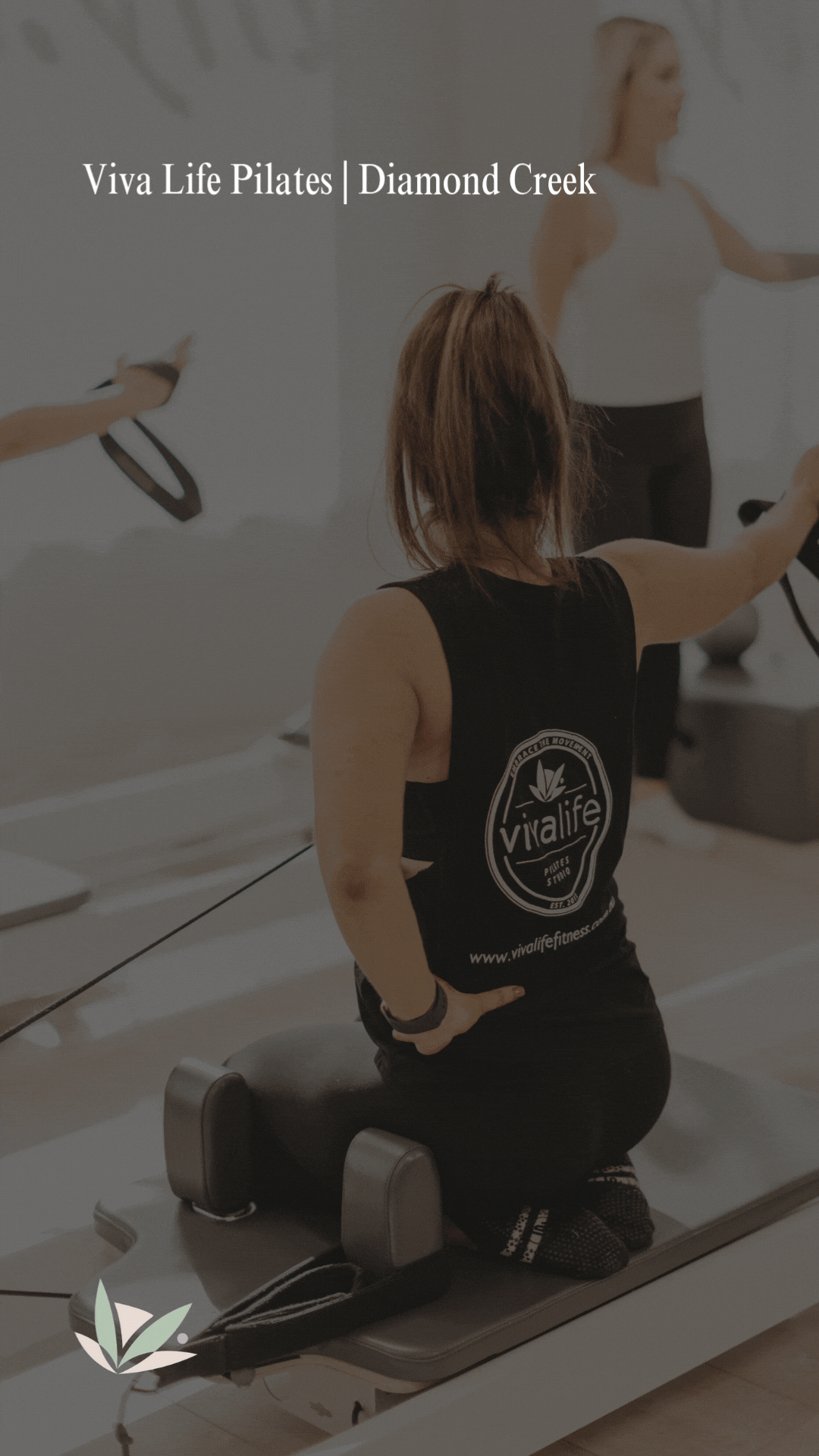 A woman participating in a Pilates class at Viva Life Pilates in Diamond Creek, kneeling on a Pilates reformer machine with her hands on her hips, wearing a black tank top and black workout pants.