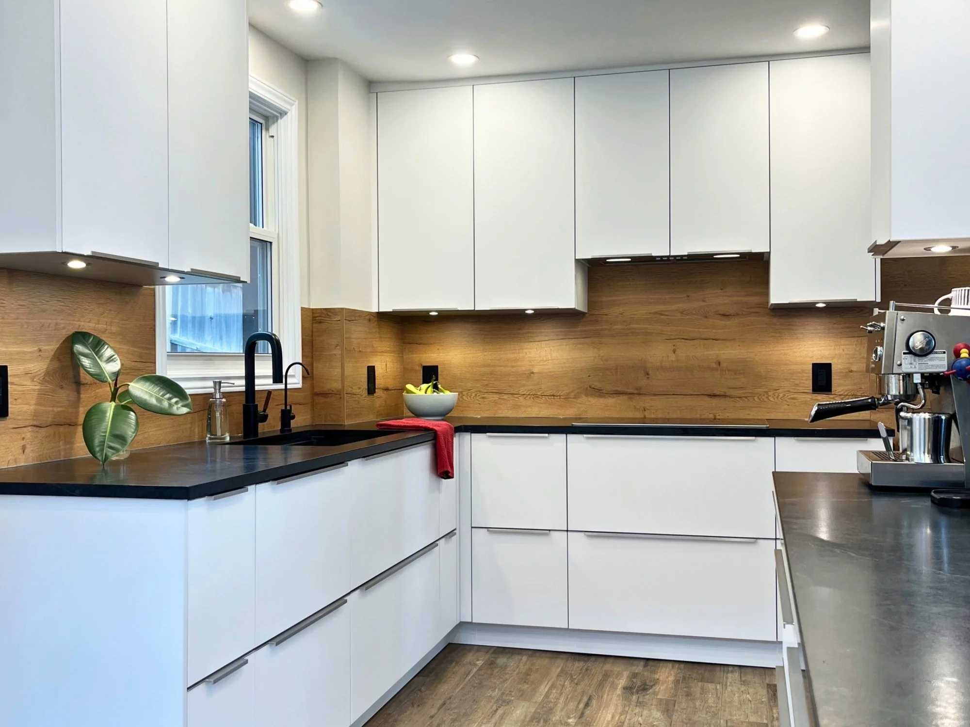 Custom white kitchen cabinets with wood backsplash panels and handleless drawers.