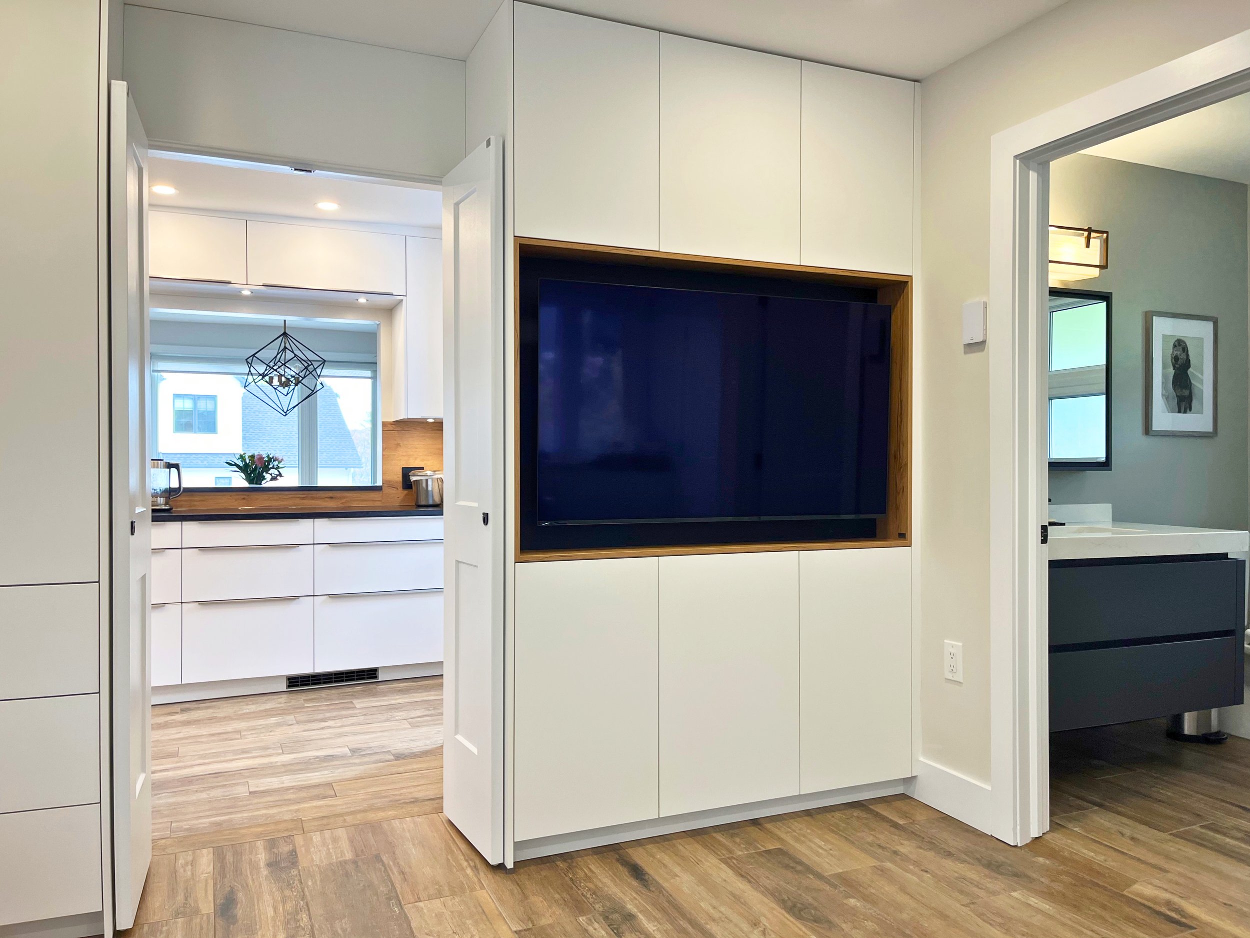 Custom TV built-in with white cabinets and wood accent.