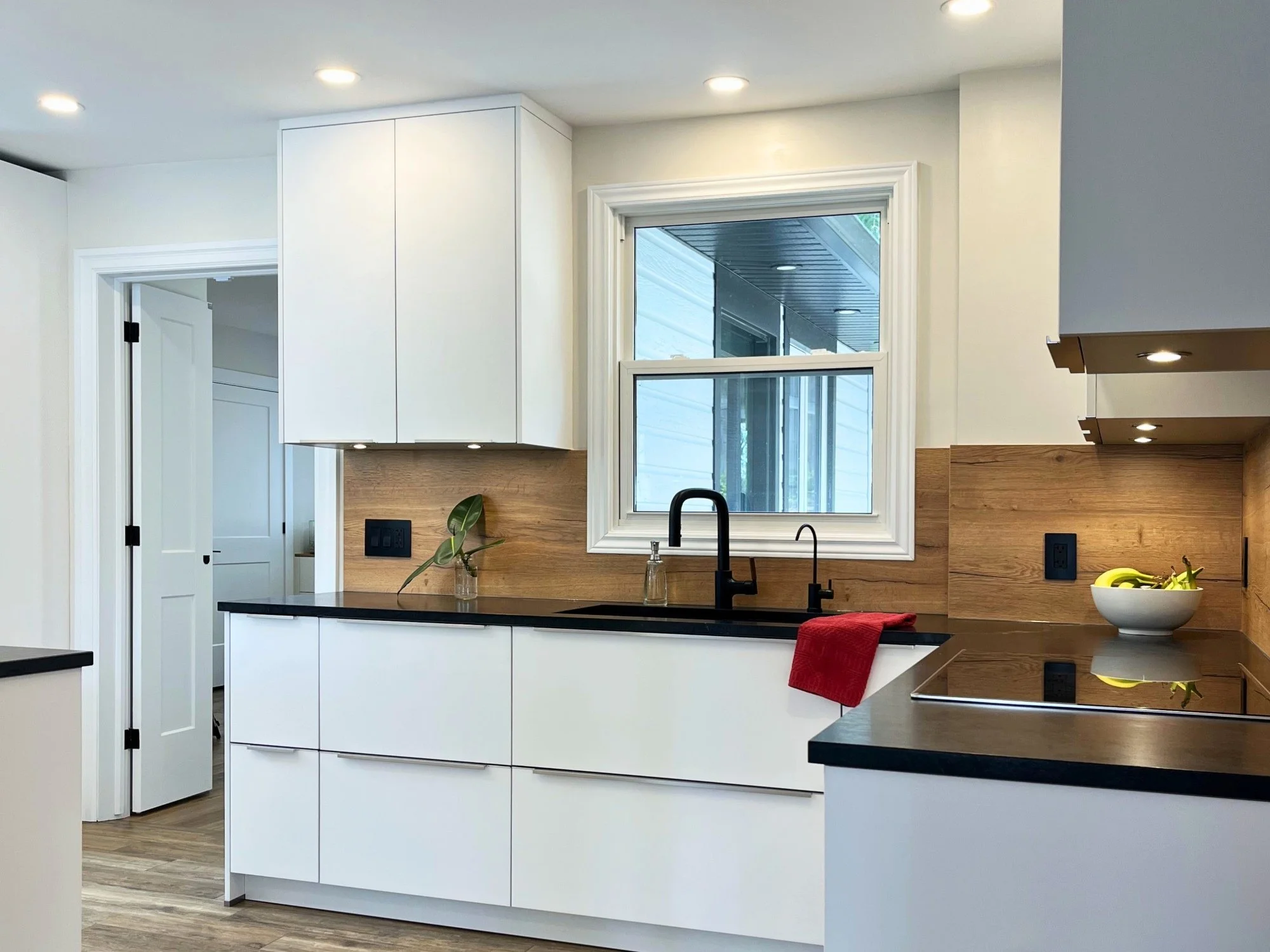 Modern white handleless kitchen with European cabinetry, black countertops, wood accents, and under-cabinet lighting.